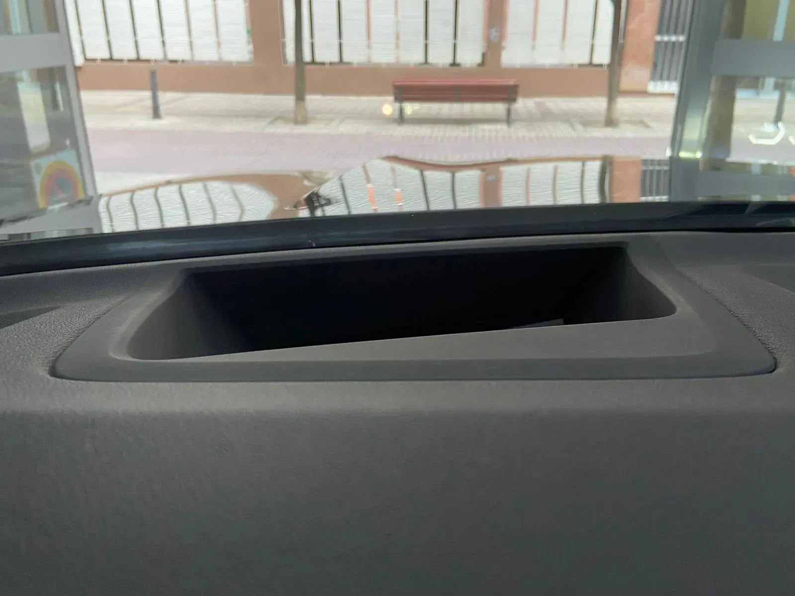 Un primer plano del tablero de instrumentos de un automóvil con un reflejo de un edificio en el parabrisas.