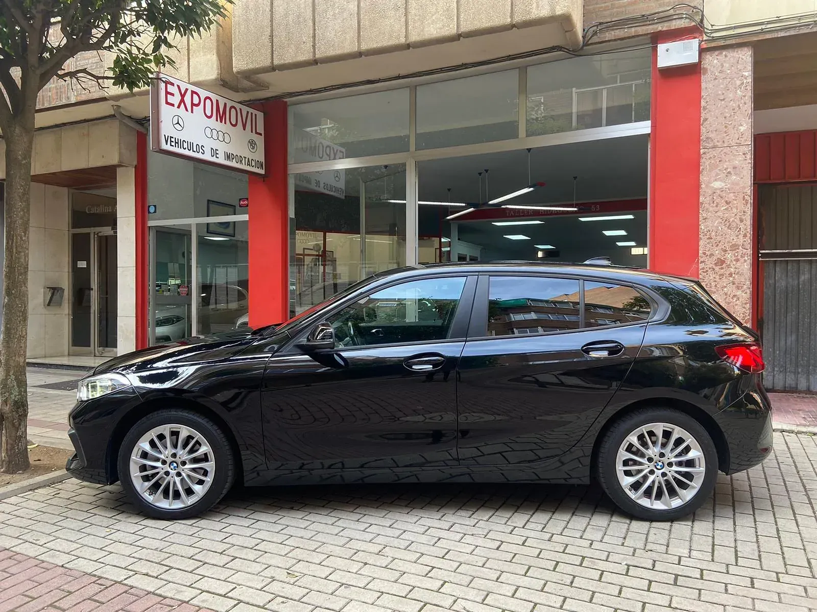 Un coche negro está aparcado delante de un concesionario de automóviles.