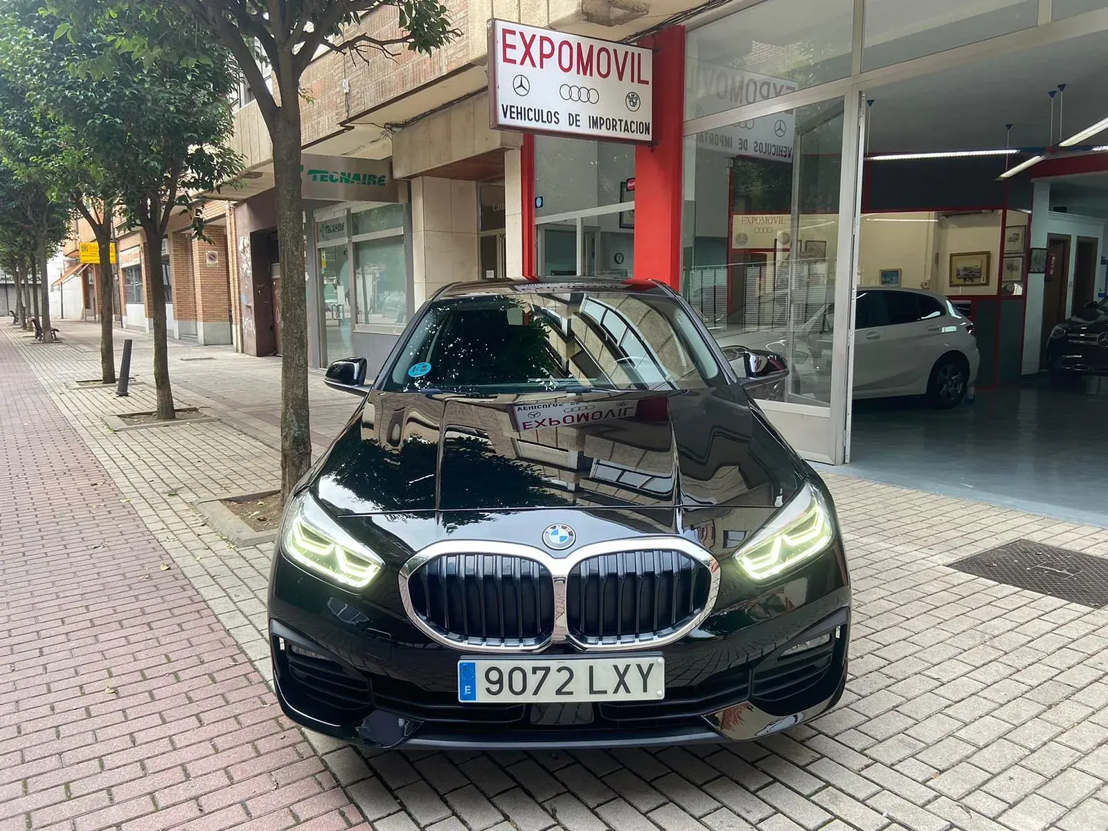 Un BMW negro está estacionado al costado de la carretera frente a un concesionario de automóviles.