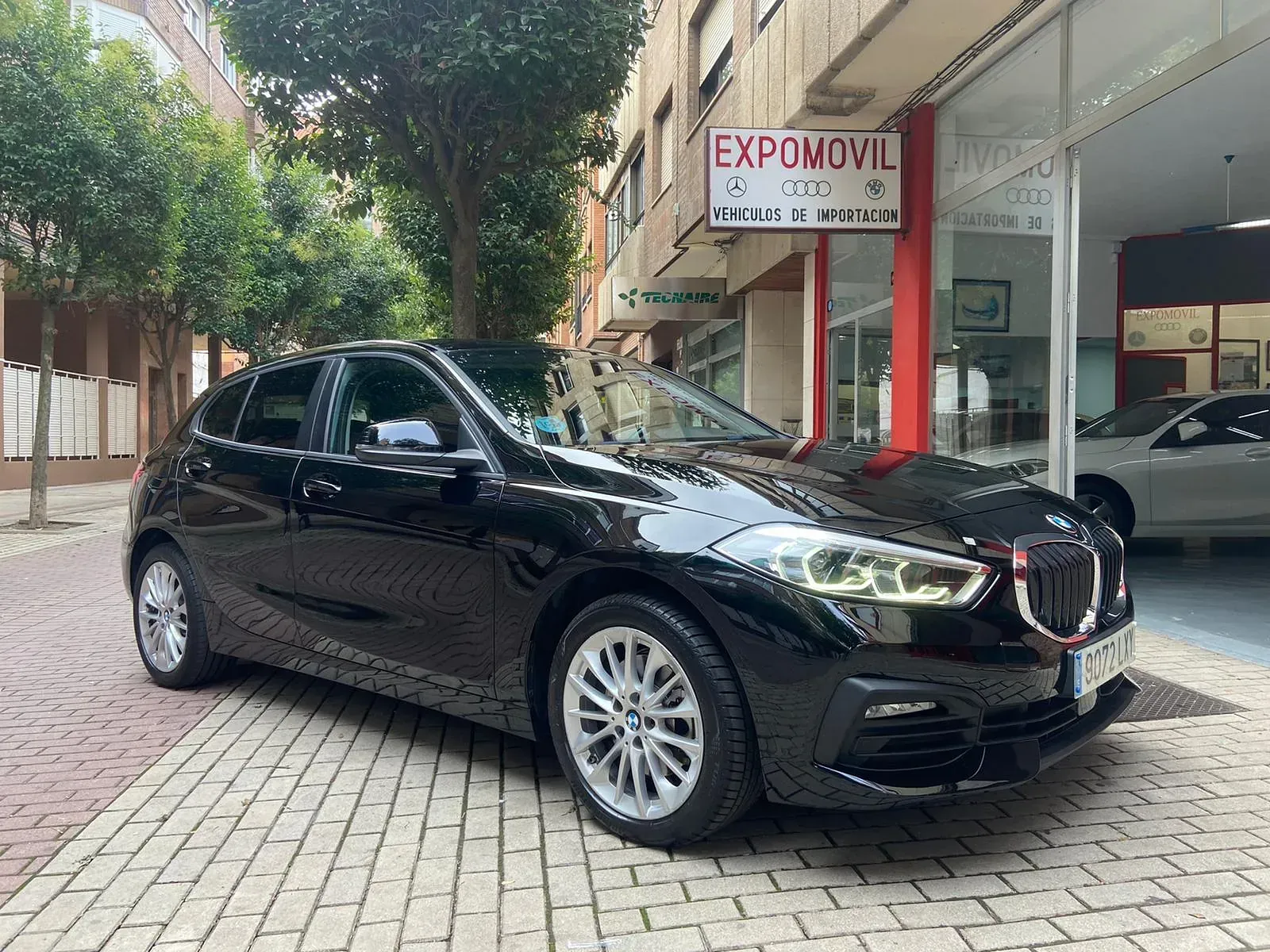 Un BMW negro está estacionado frente a un concesionario de automóviles.