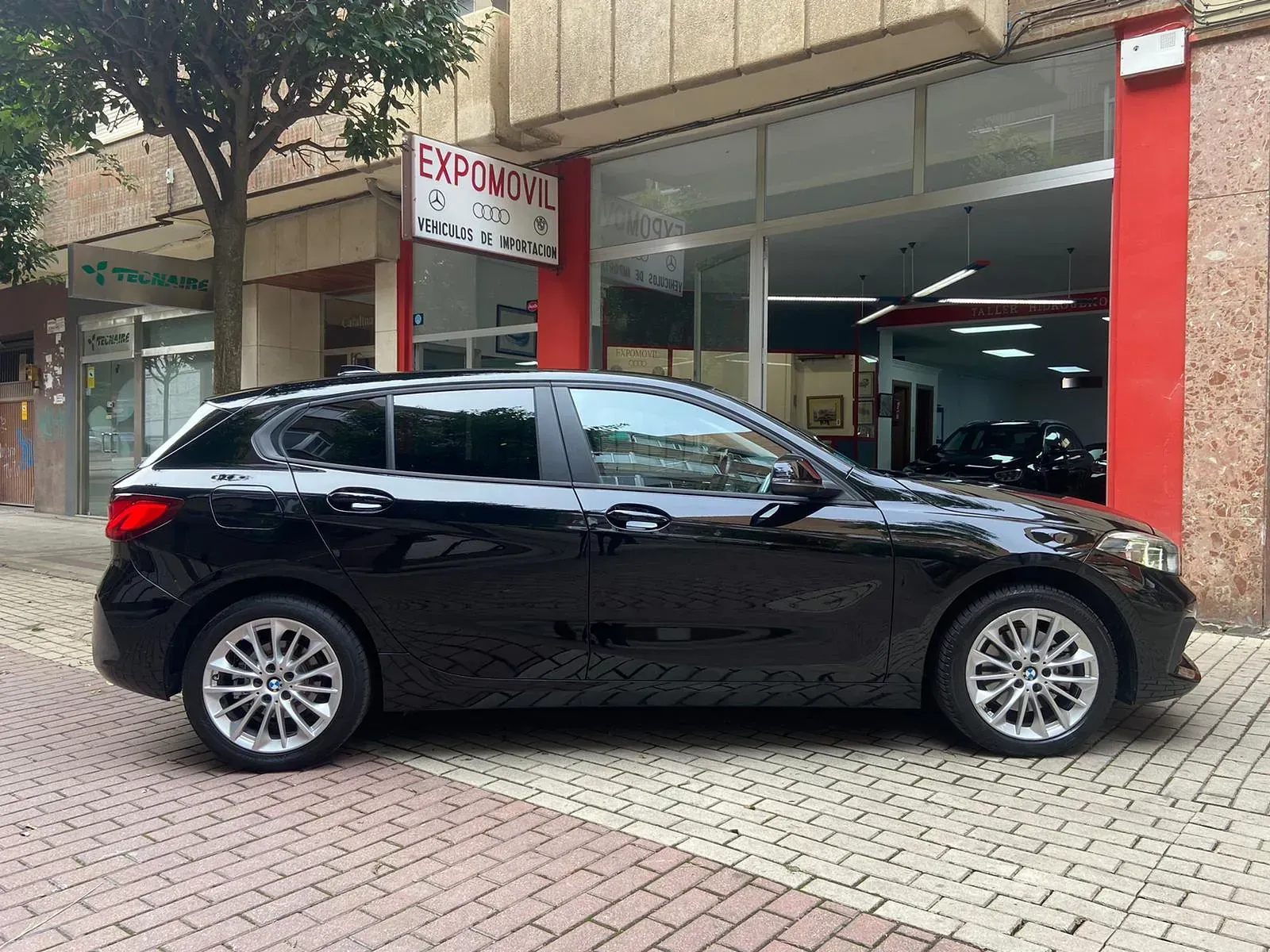 Un coche negro está aparcado delante de un concesionario de automóviles.