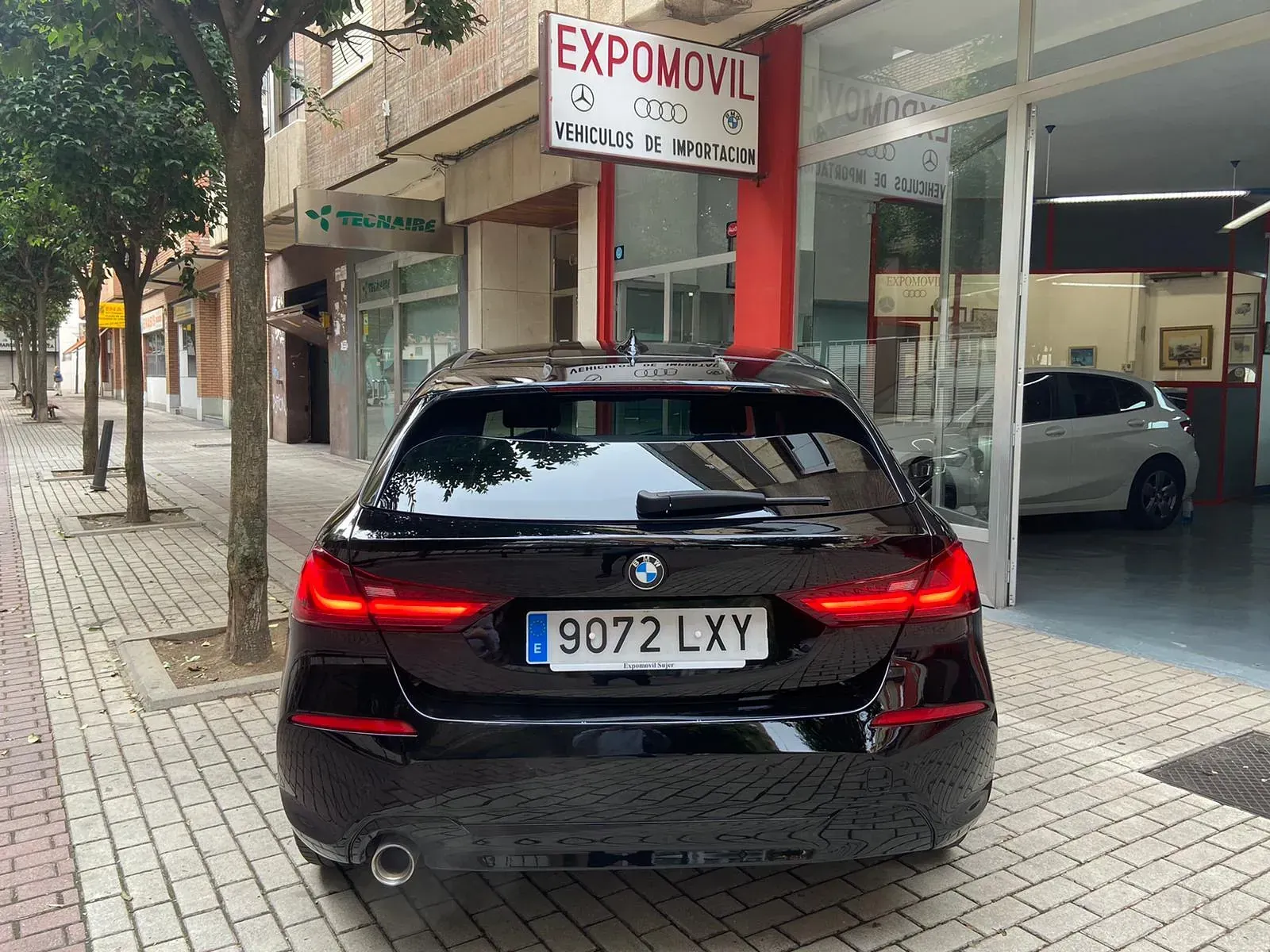 Un BMW negro está estacionado frente a un concesionario de automóviles.