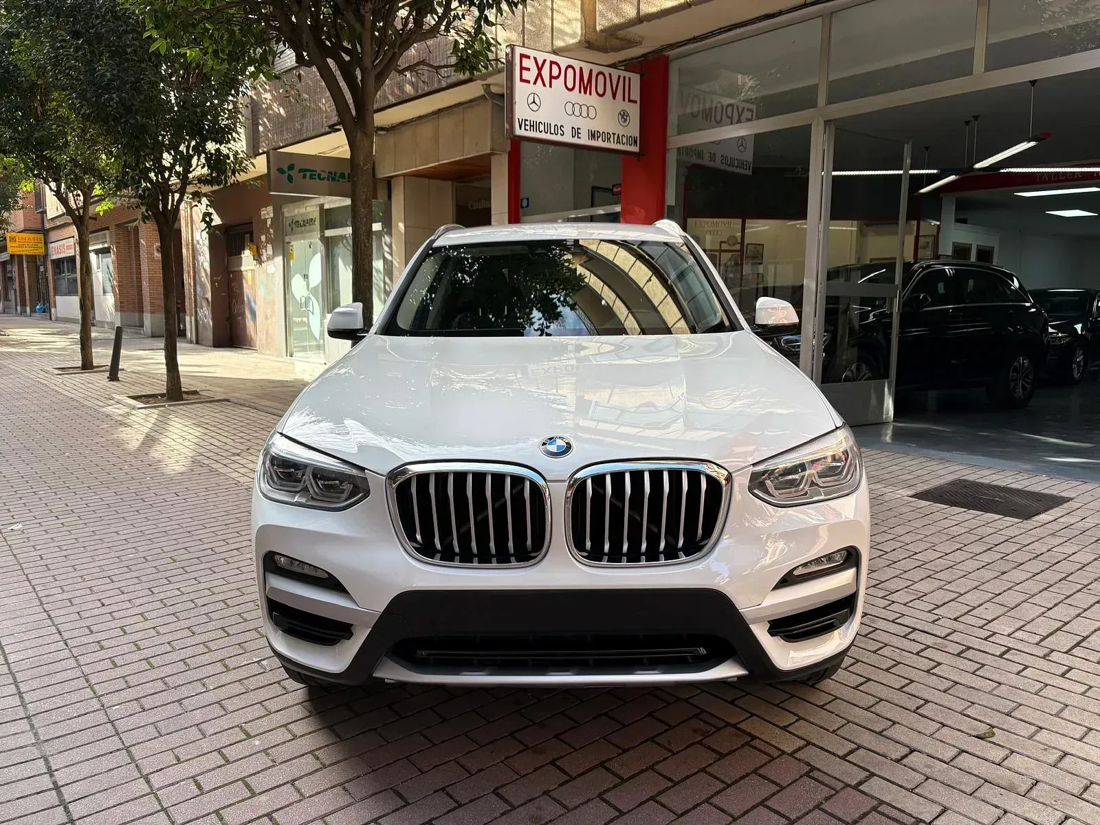 Un BMW X3 blanco está estacionado frente a un concesionario de automóviles.