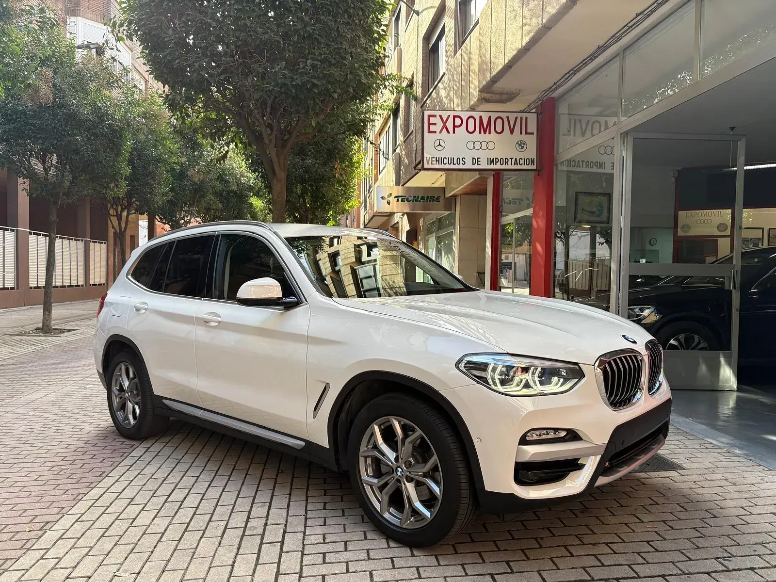 Un BMW X3 blanco está estacionado frente a un concesionario de automóviles.