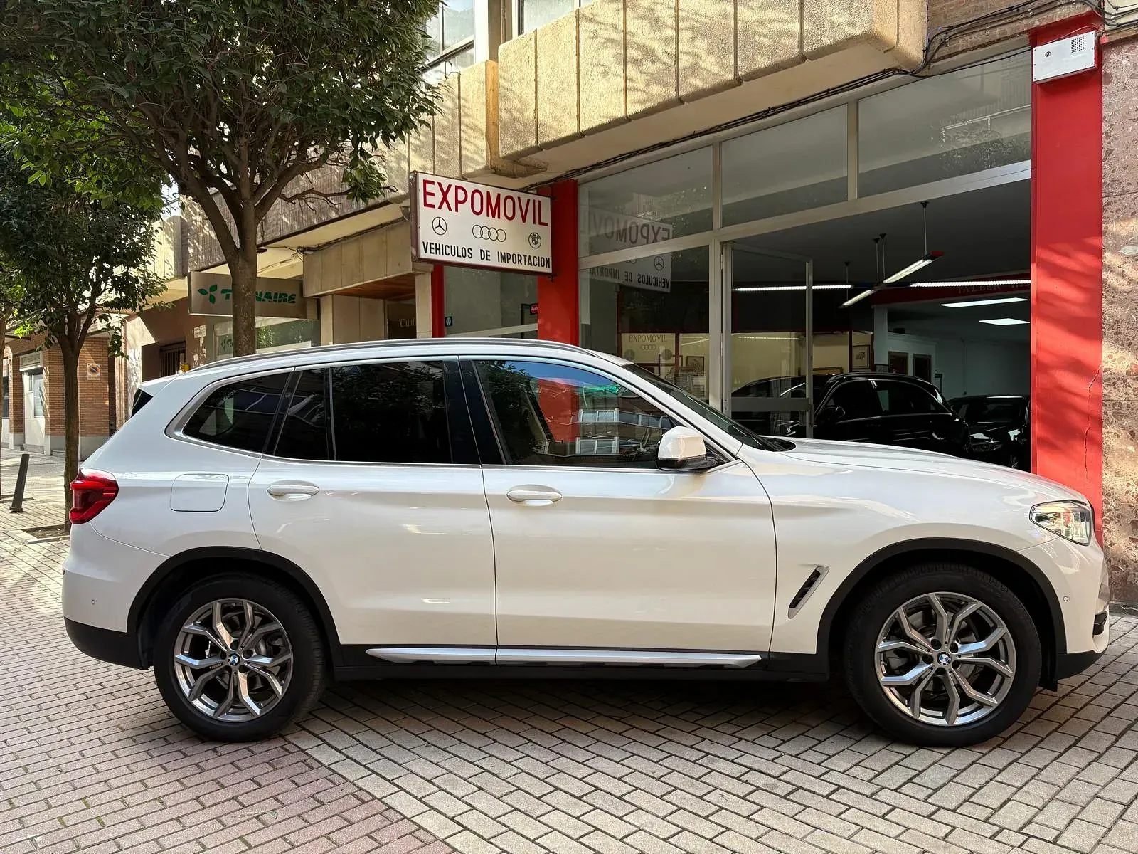 Un BMW X3 blanco está estacionado frente a un concesionario de automóviles.