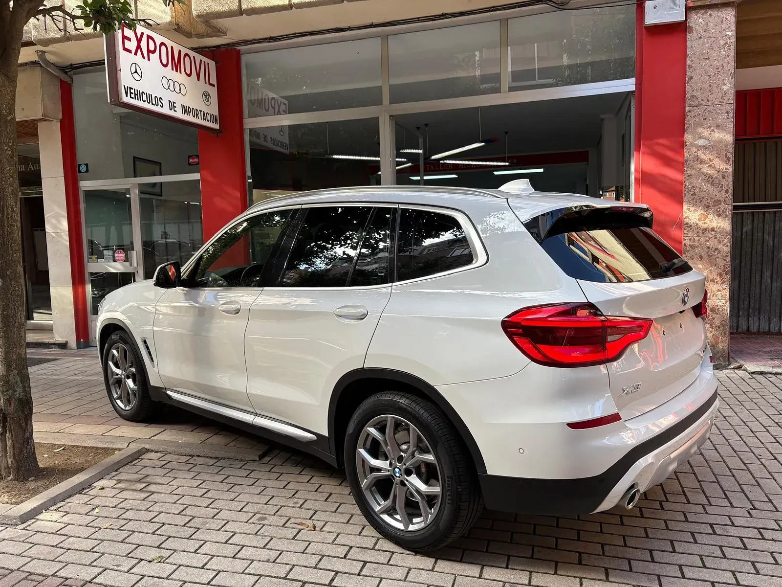 Un BMW X3 blanco está estacionado frente a un concesionario de automóviles.