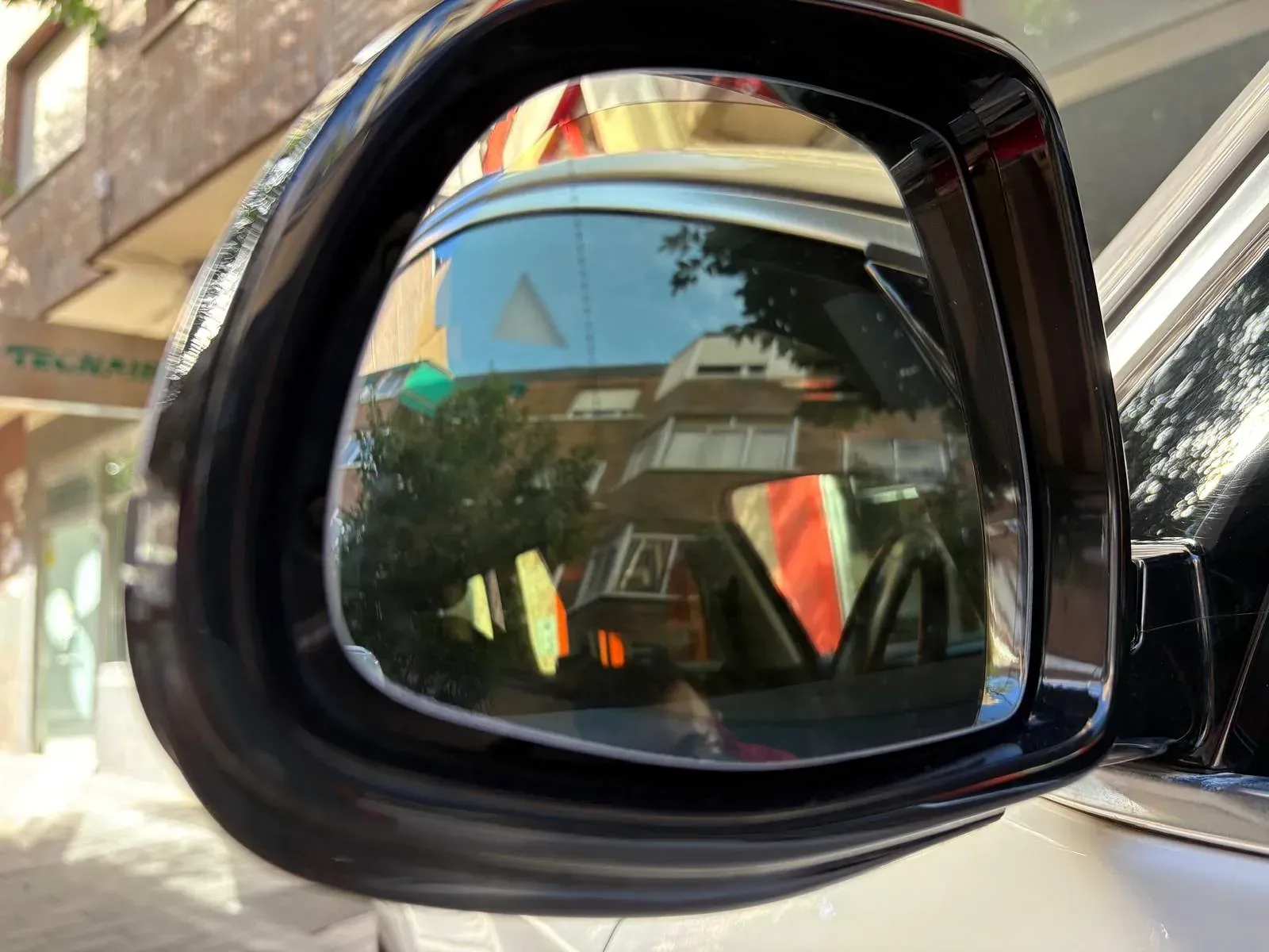 Un primer plano del espejo retrovisor de un automóvil con un edificio al fondo.