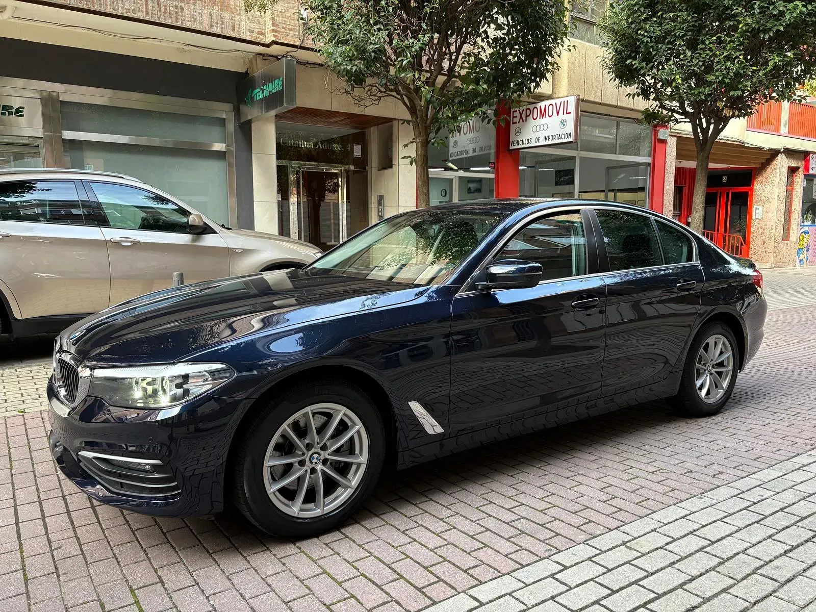 Un coche azul está estacionado en una acera de ladrillos frente a un edificio.