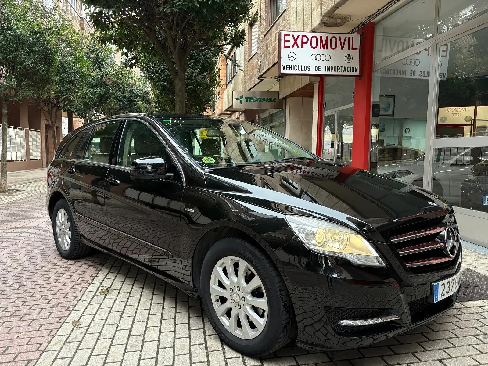 Un coche negro está aparcado delante de un concesionario de automóviles.