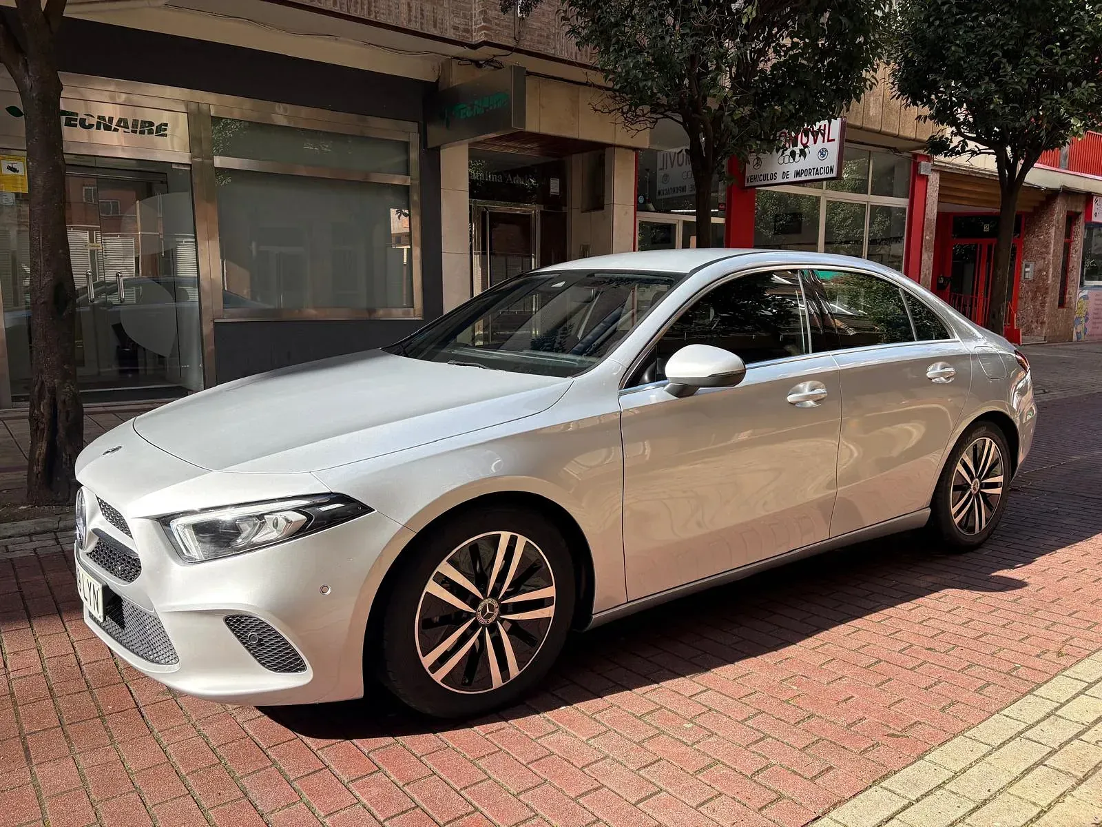 Un coche plateado está aparcado en una acera de ladrillos frente a un edificio.
