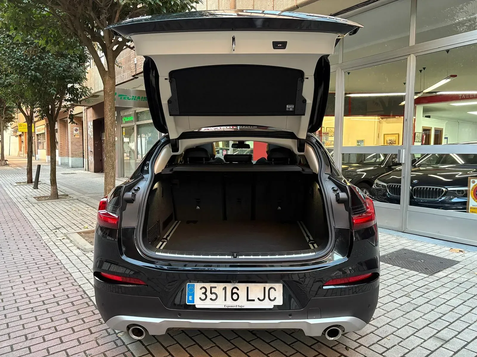 Un coche negro con el maletero abierto está estacionado en una acera de ladrillos.