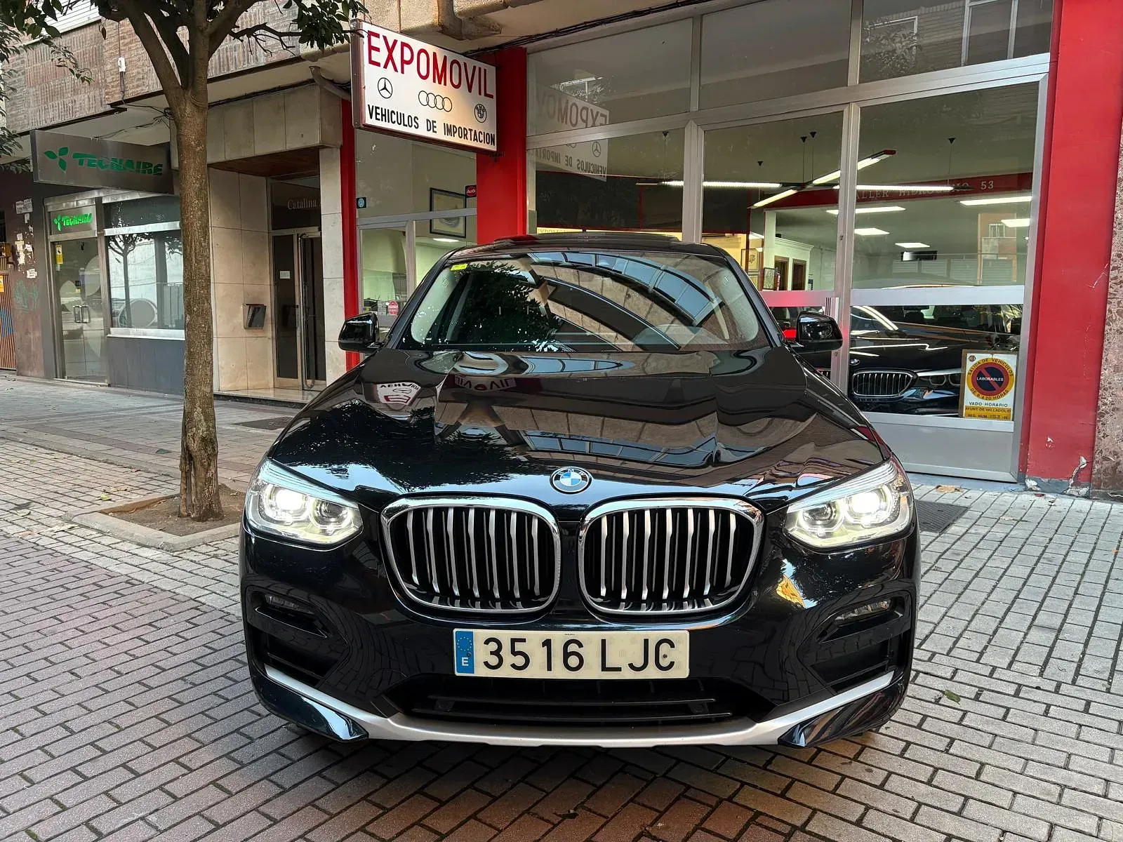 Un BMW X3 negro está estacionado frente a un concesionario de automóviles.