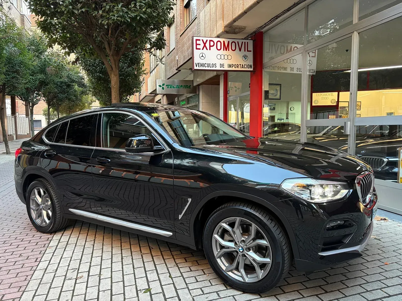 Un BMW X4 negro está estacionado frente a un concesionario de automóviles.