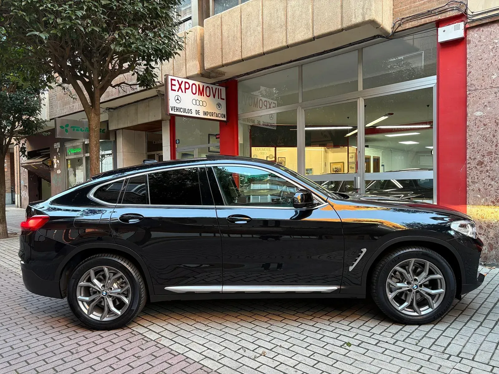 Un BMW X4 negro está estacionado frente a un concesionario de automóviles.