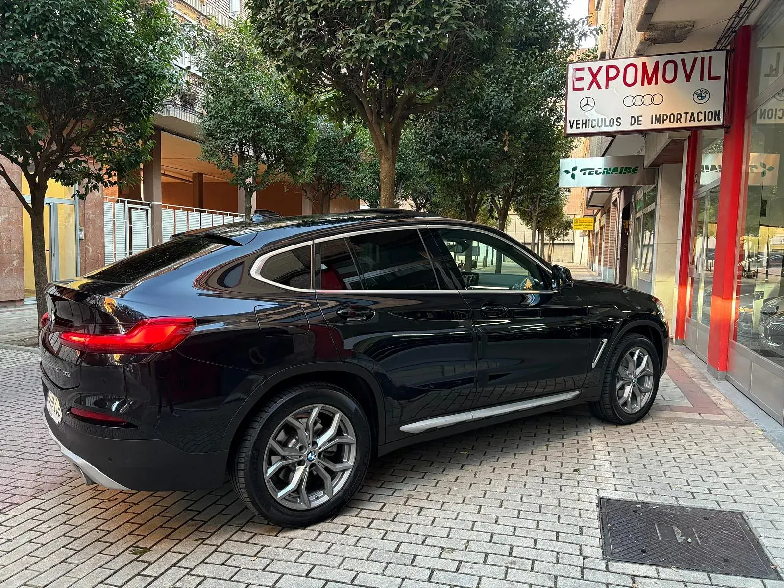 Un coche negro está estacionado en una acera de ladrillos frente a un edificio.