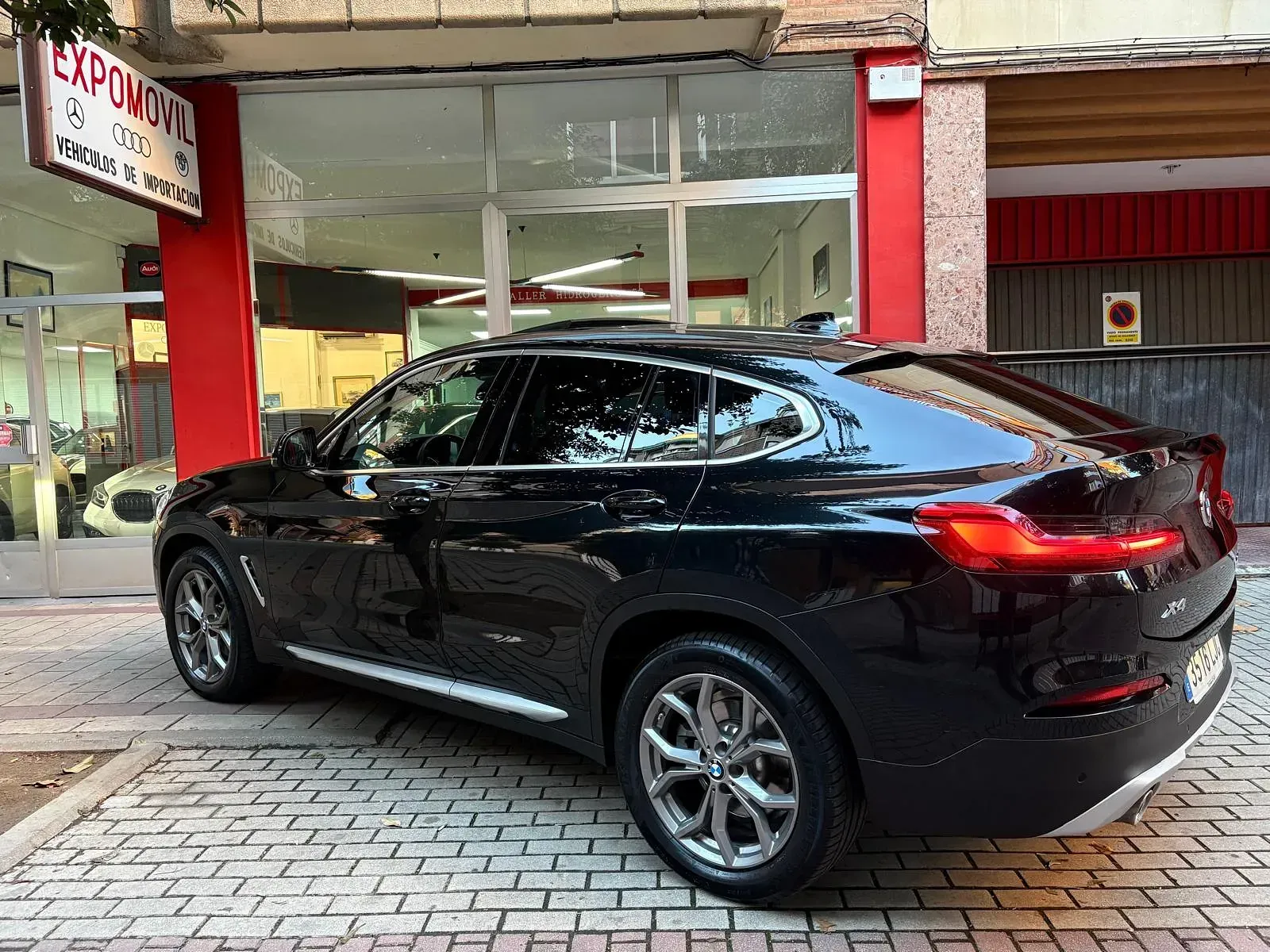 Un BMW X4 negro está estacionado frente a un concesionario de automóviles.