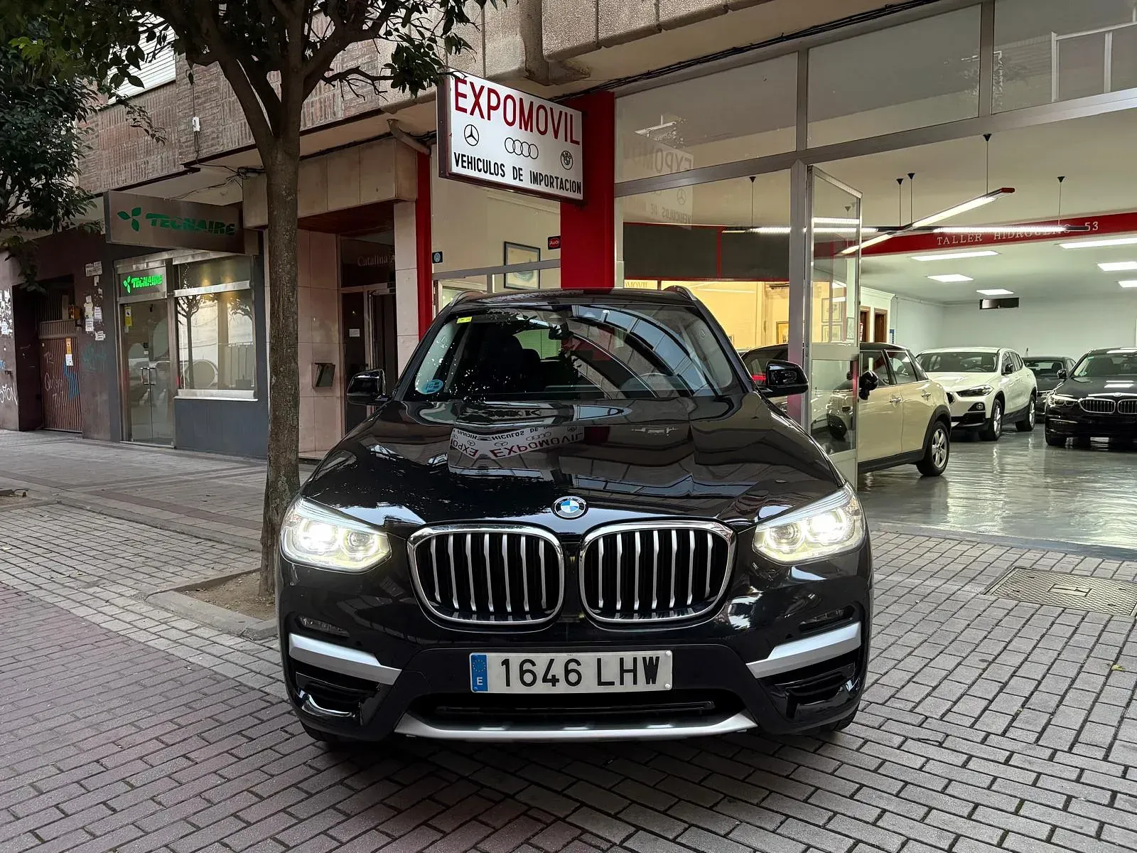 Un BMW X3 negro está estacionado frente a un concesionario de automóviles.