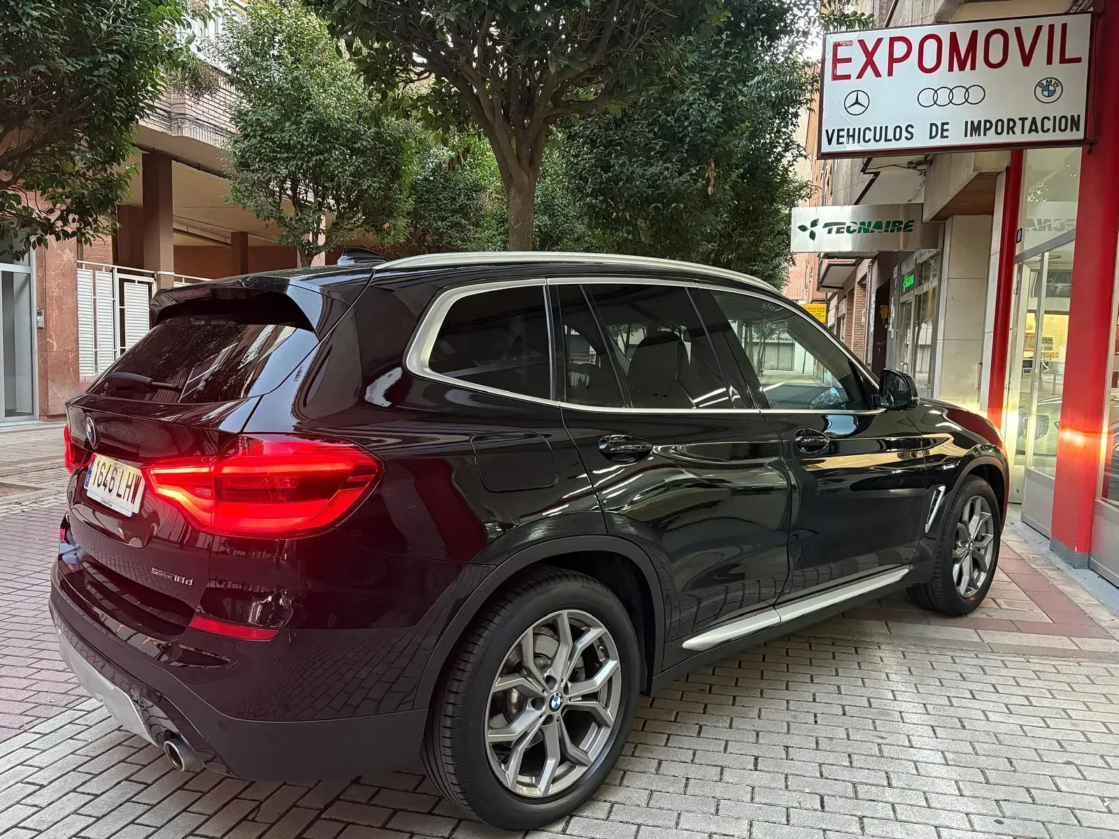 Un BMW X3 negro está estacionado frente a un concesionario de automóviles.