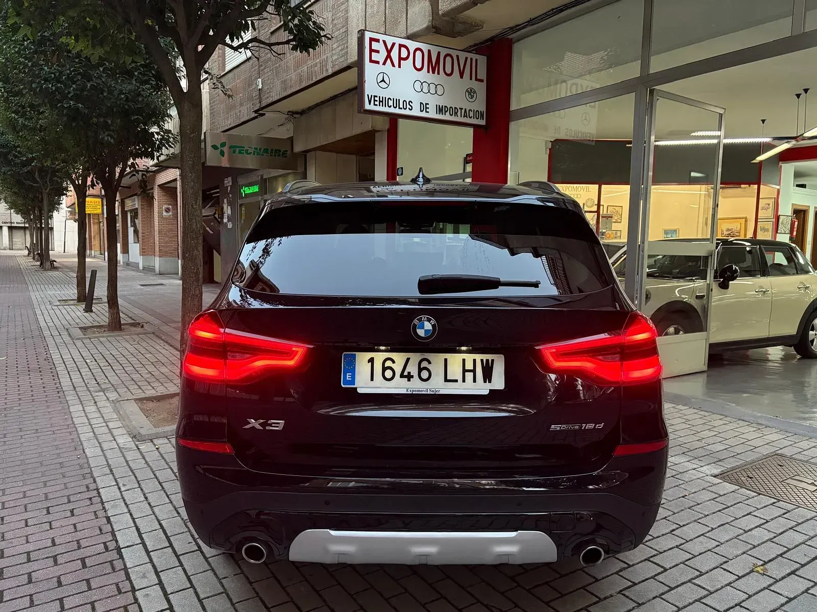 Un BMW X3 negro está estacionado frente a un concesionario de automóviles.
