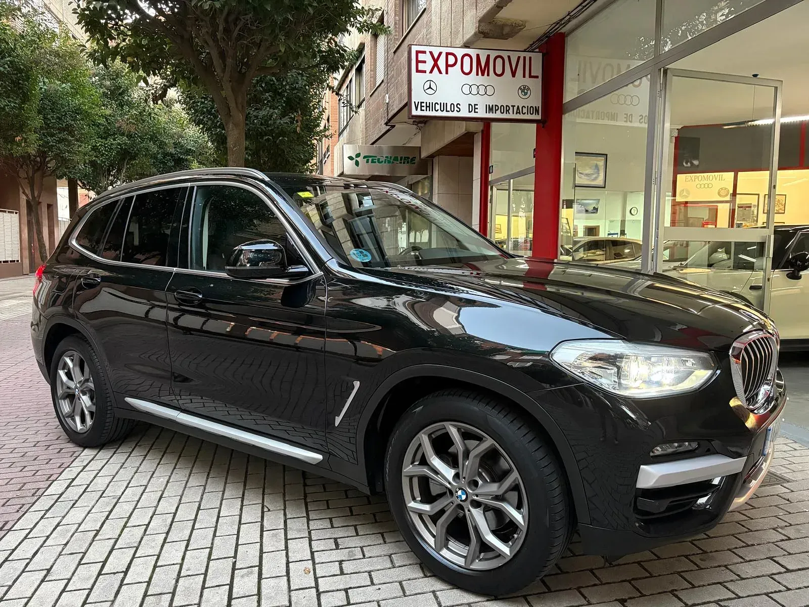 Un BMW X3 negro está estacionado frente a un concesionario de automóviles.