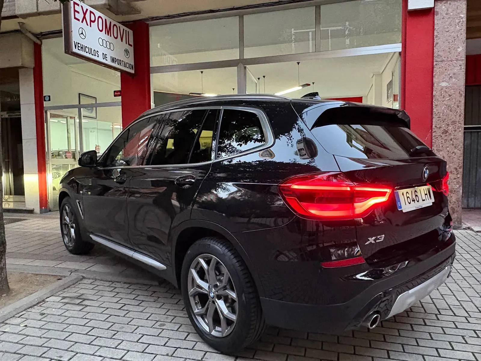 Un BMW X3 negro está estacionado frente a un concesionario de automóviles.
