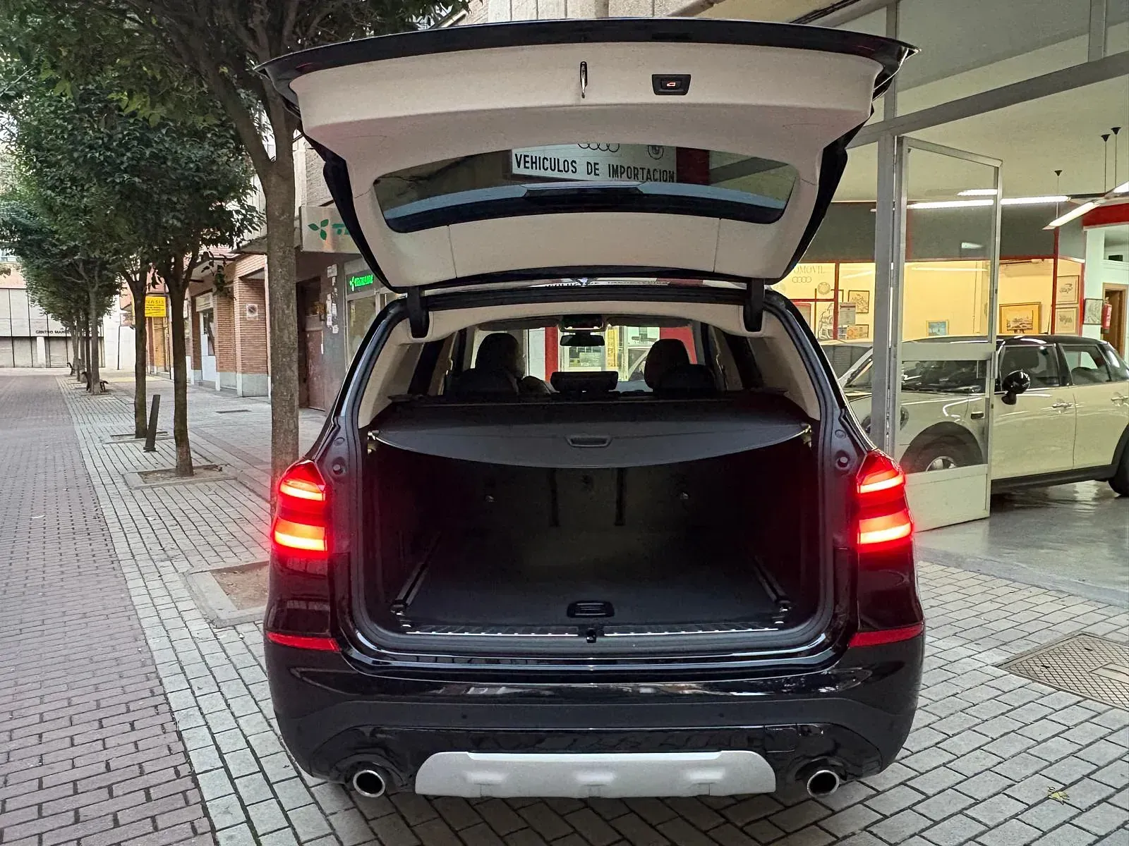 Un todoterreno negro con el maletero abierto está estacionado frente a un edificio.