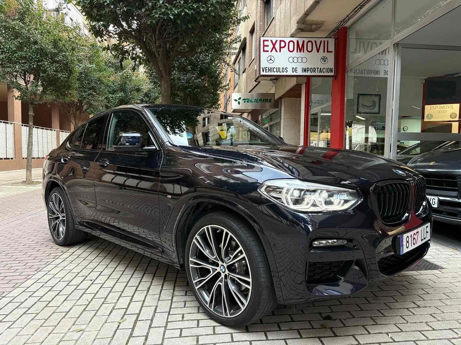 Un BMW X4 negro está estacionado frente a un concesionario de automóviles.