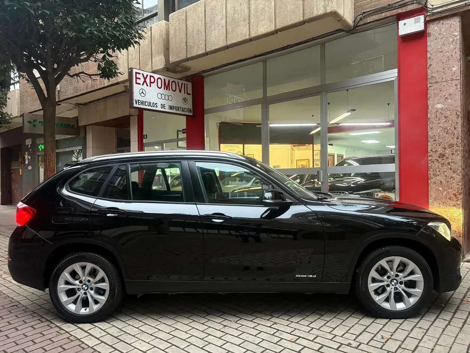 Un BMW X1 negro está estacionado frente a un concesionario de automóviles.