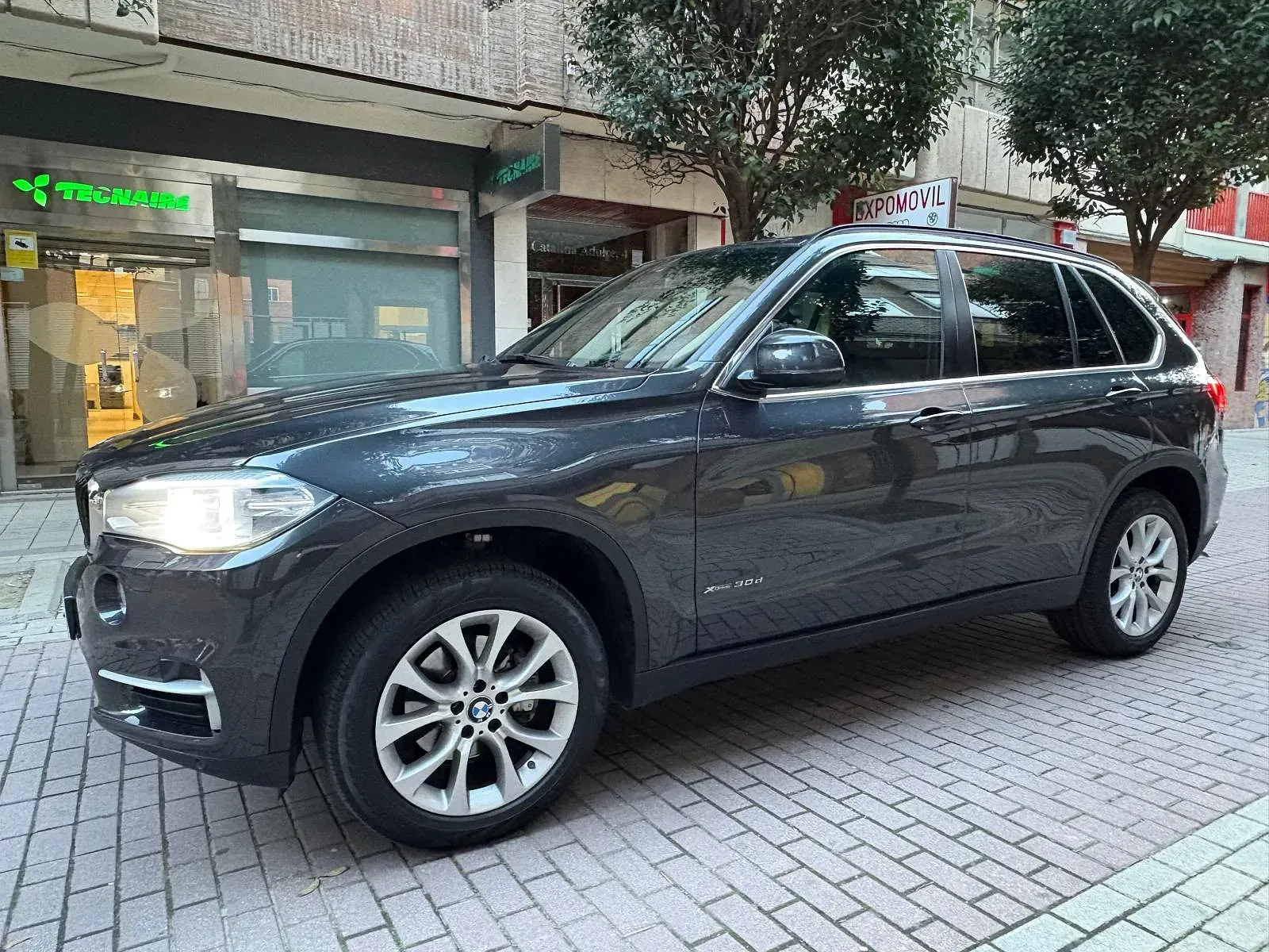 Un BMW X5 está estacionado en una acera de ladrillos frente a un edificio.