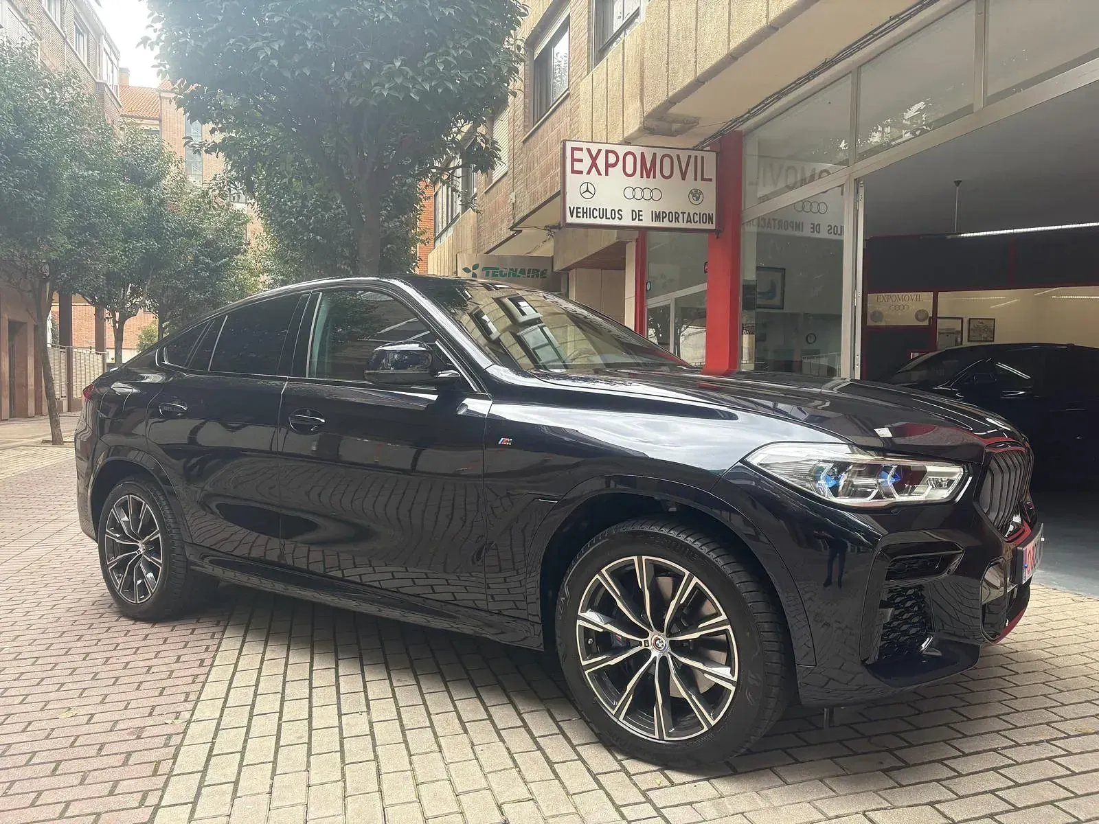 Un BMW X6 negro está estacionado frente a un concesionario de automóviles.