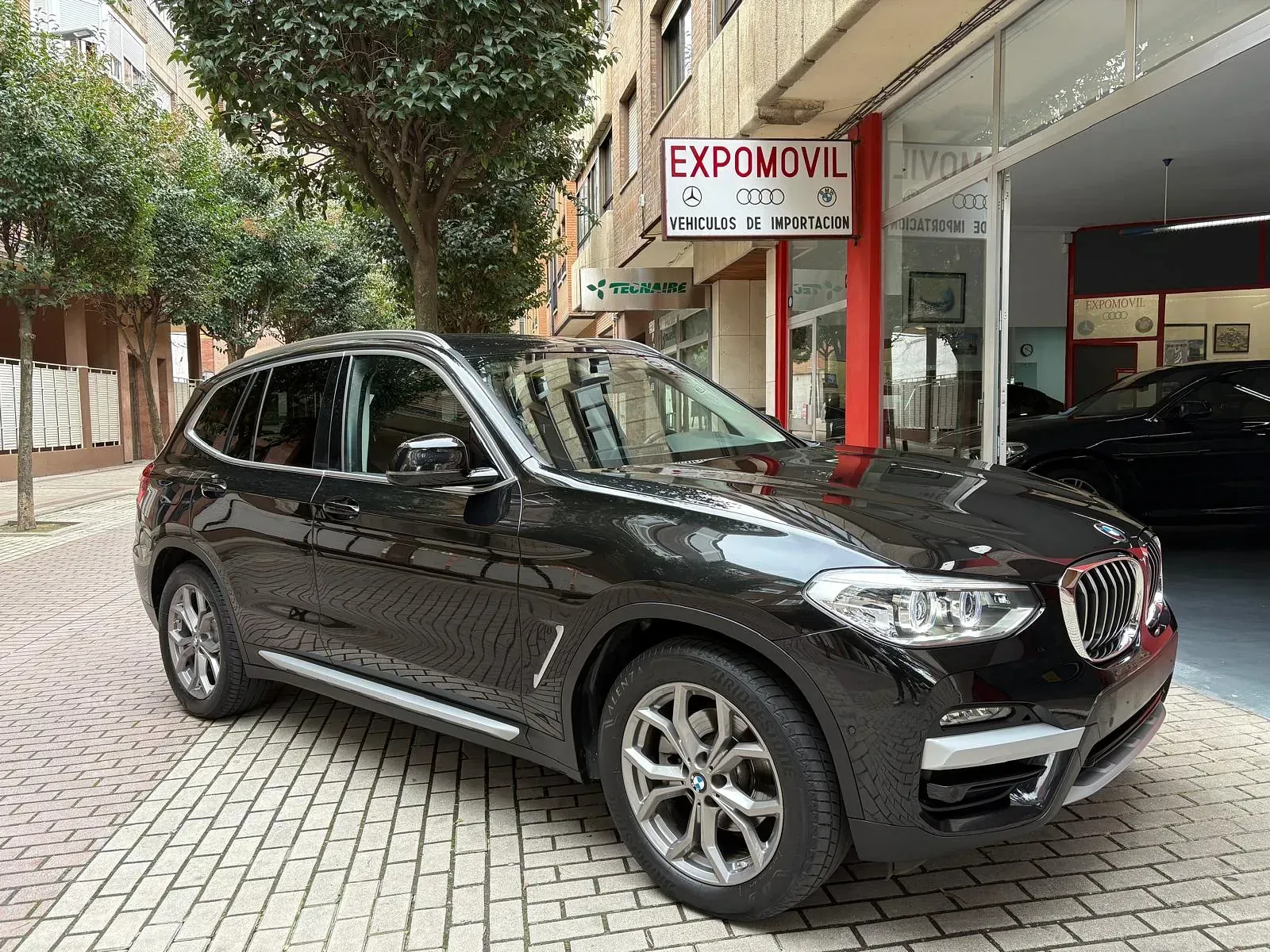 Un BMW X3 negro está estacionado frente a un concesionario de automóviles.