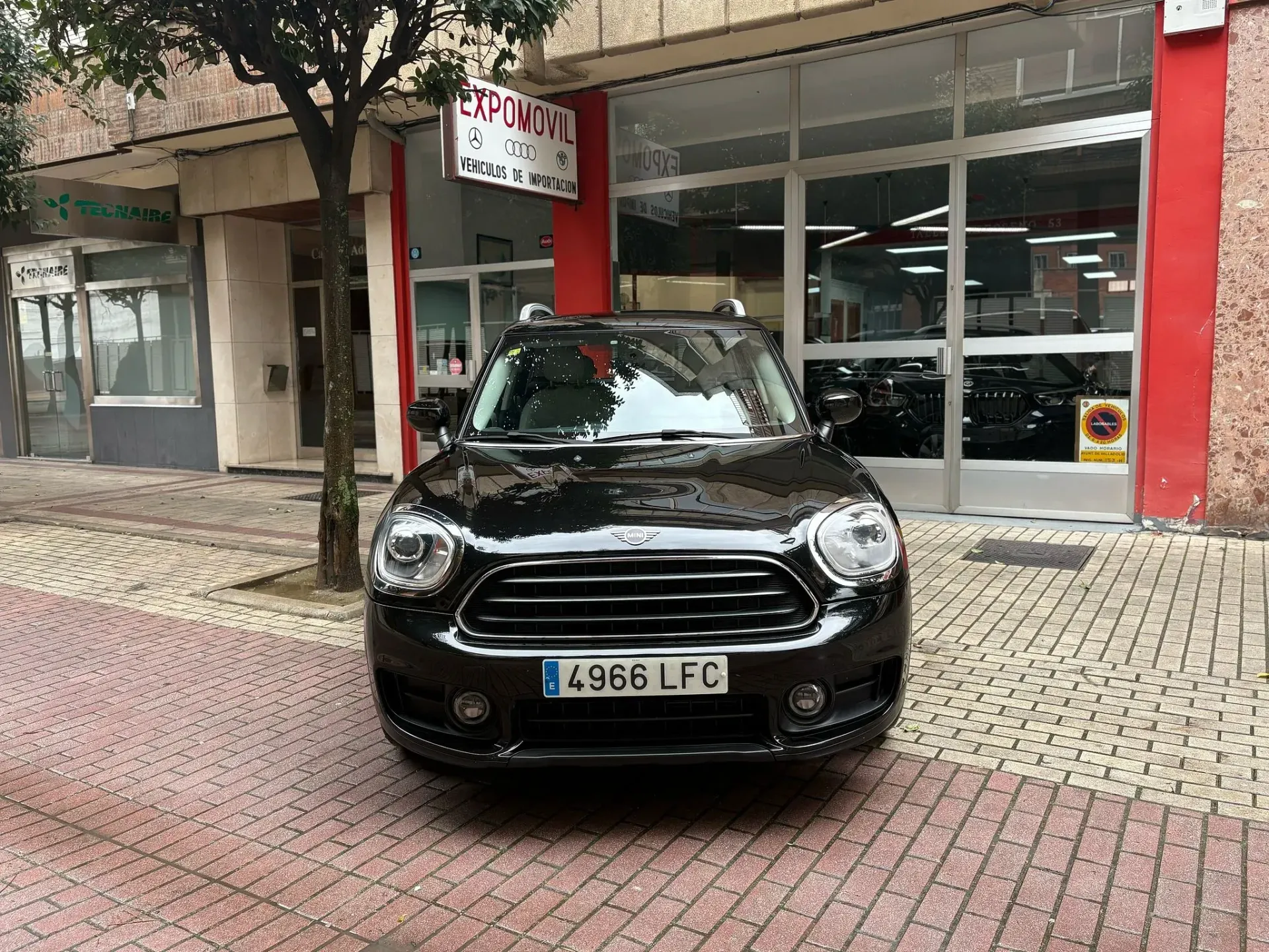 Un Mini Cooper negro está estacionado frente a un concesionario de automóviles.