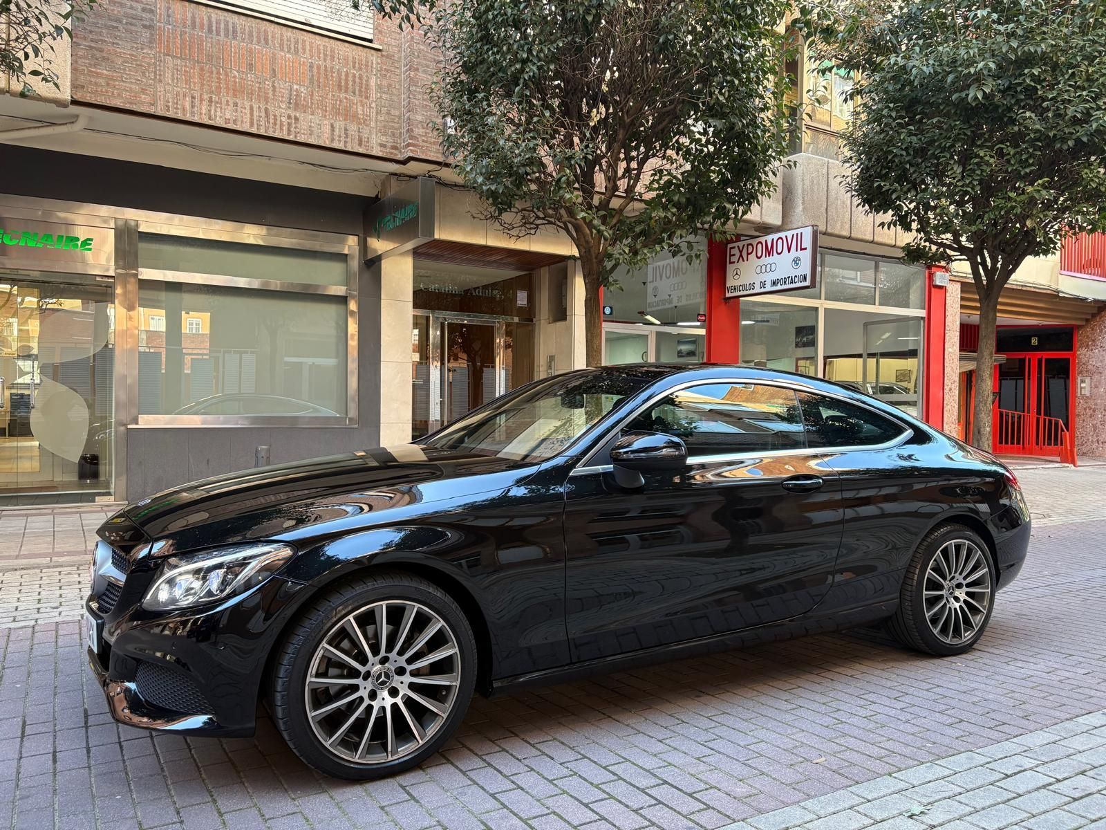 Un coche negro está estacionado en una acera de ladrillos frente a un edificio.