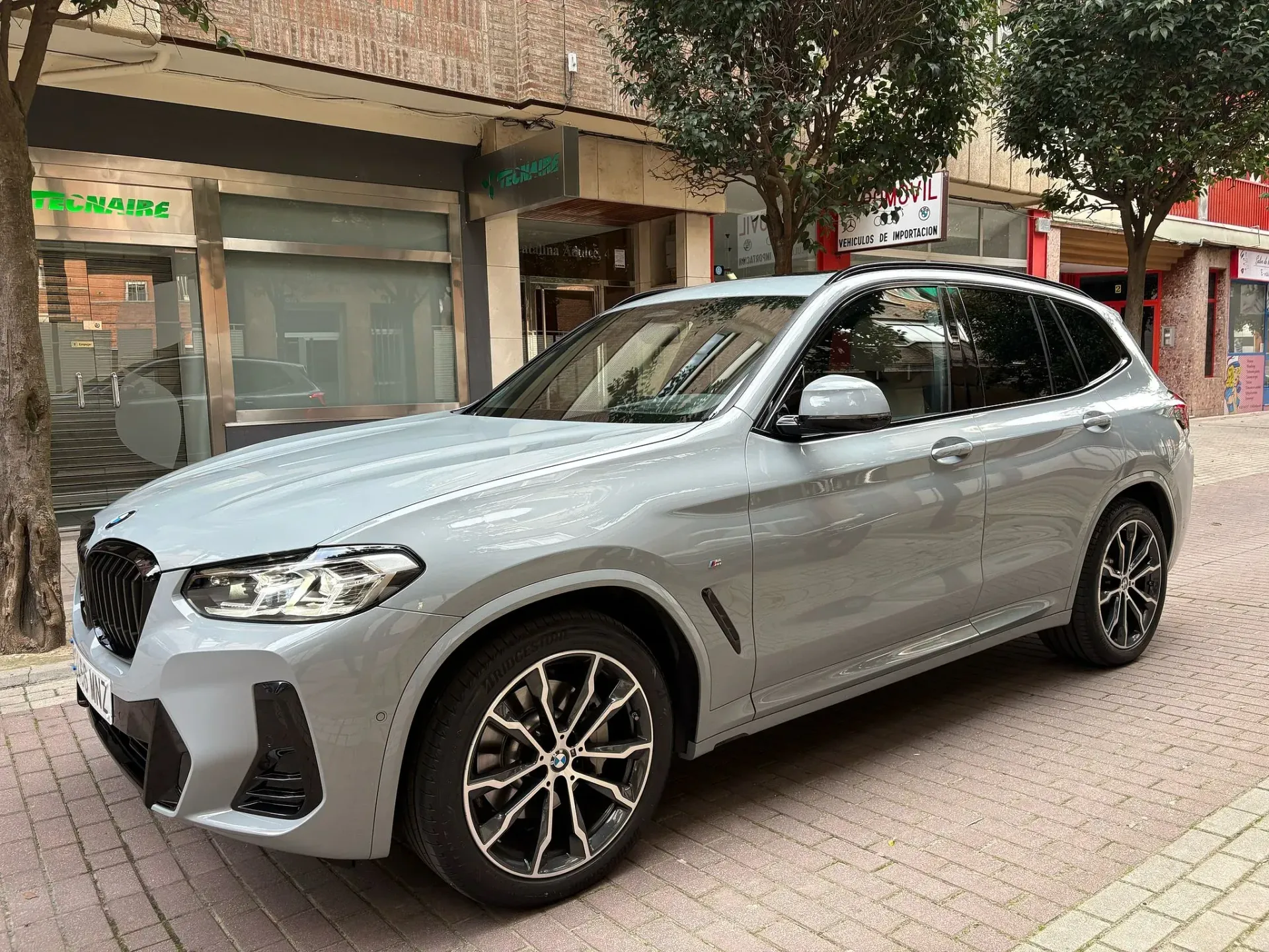 Un BMW X3 gris está estacionado en una acera frente a un edificio.