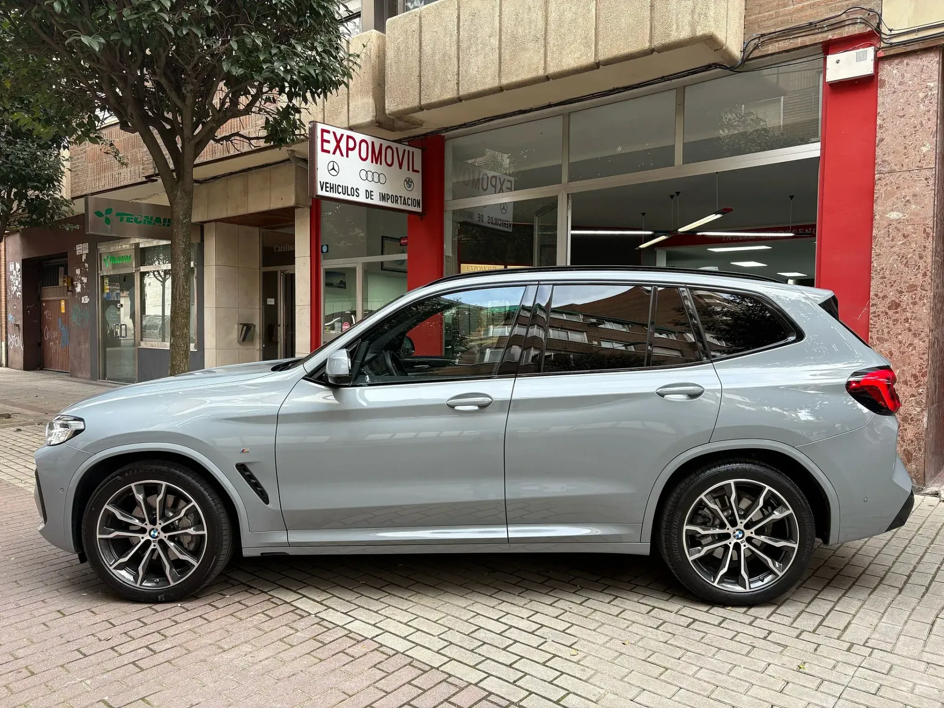 Un BMW X3 está estacionado frente a un concesionario de automóviles.