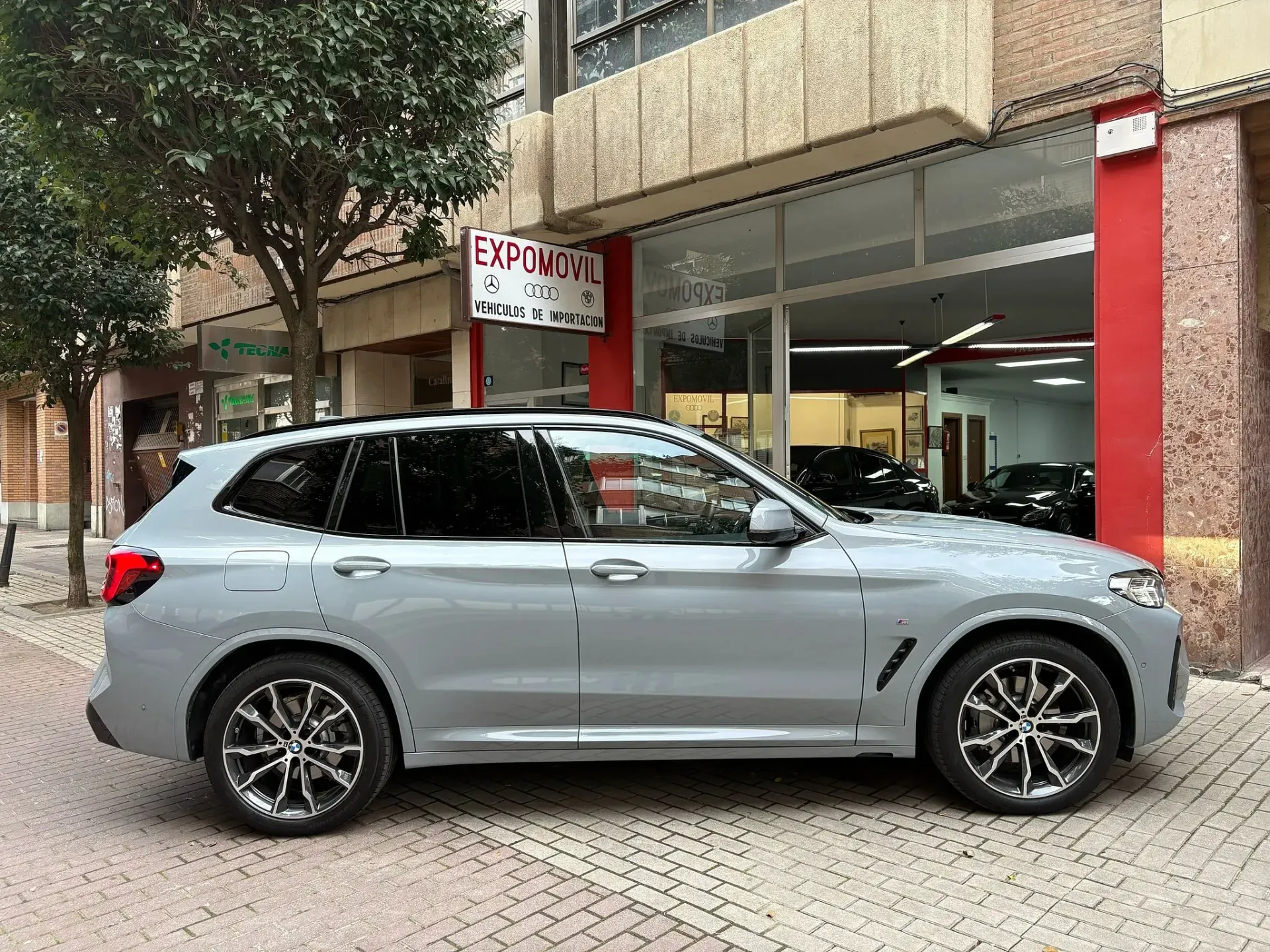Un BMW X3 está estacionado frente a un concesionario de automóviles.