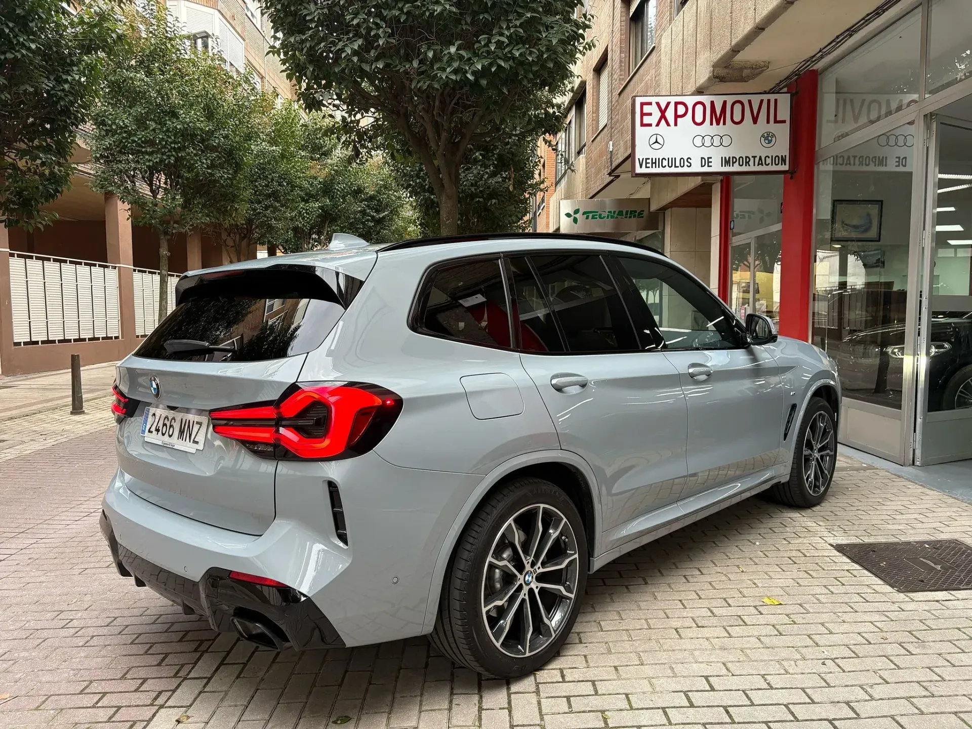 Un BMW X3 gris está estacionado frente a un concesionario de automóviles.