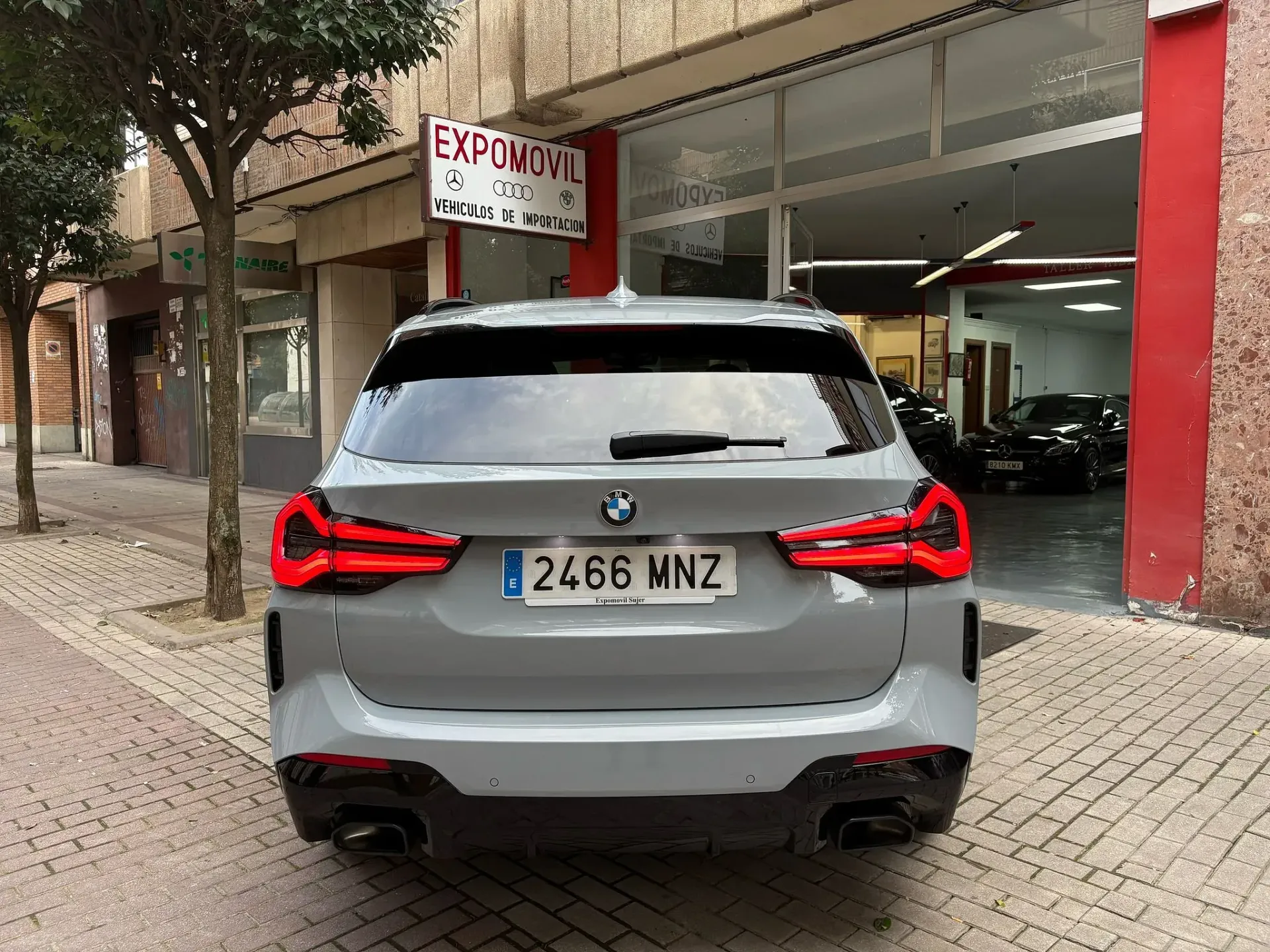 Un BMW gris está estacionado frente a un concesionario de automóviles.