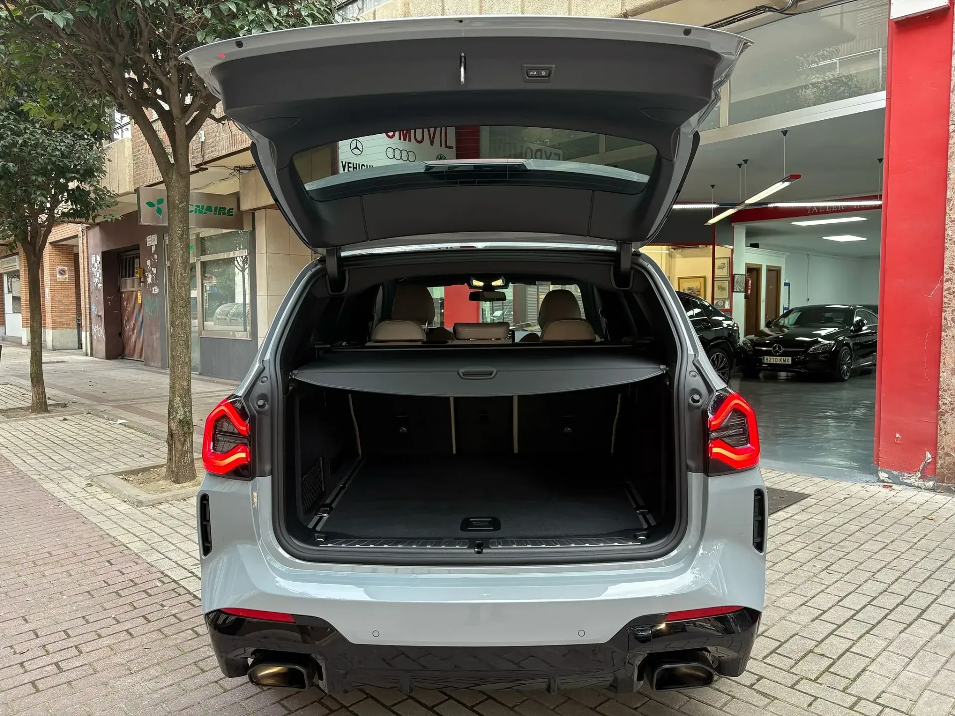 La parte trasera de un coche con el maletero abierto está aparcado delante de un concesionario de automóviles.