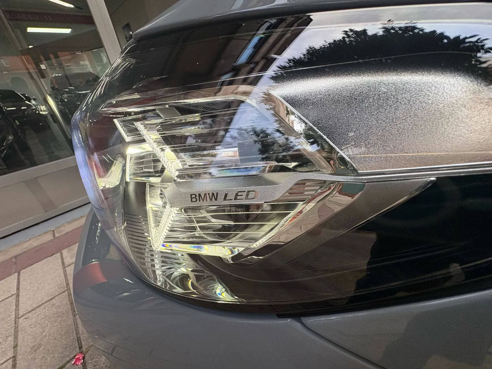 Un primer plano del faro de un automóvil con el reflejo de un edificio en él.