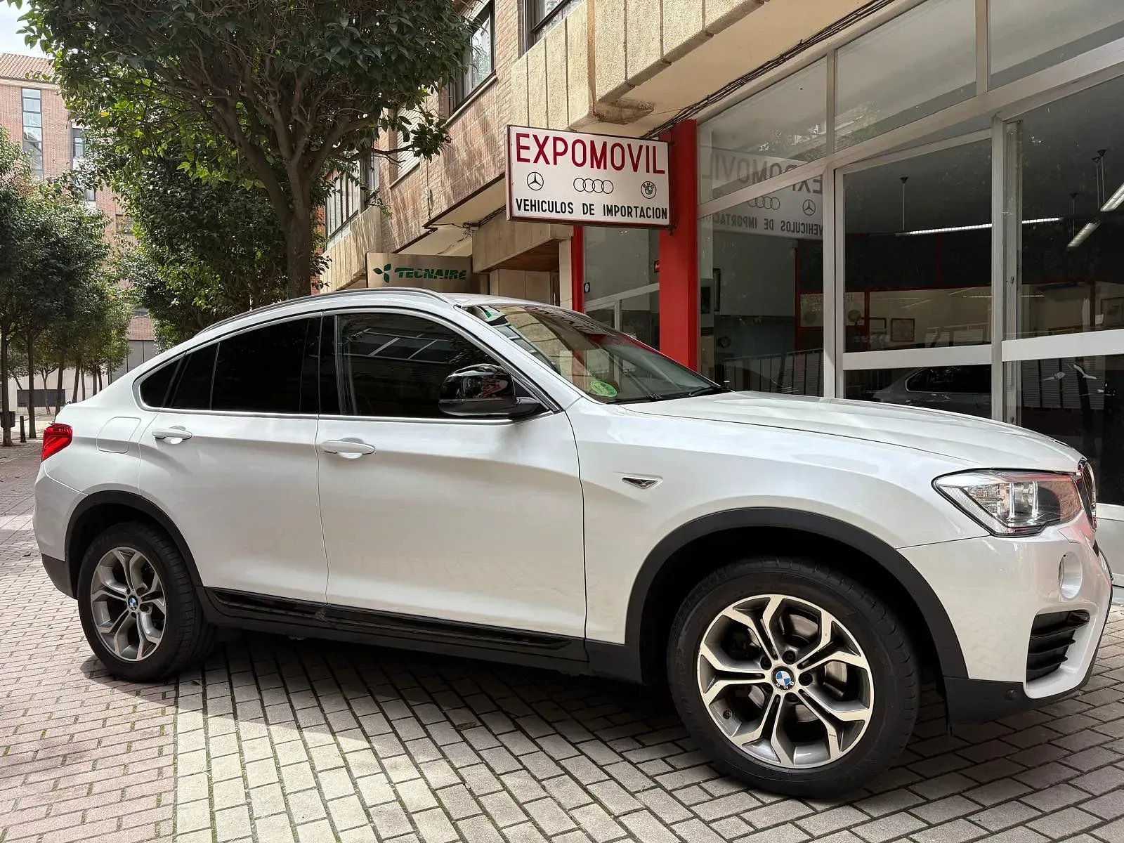 Un BMW X4 blanco está estacionado frente a un concesionario de automóviles.