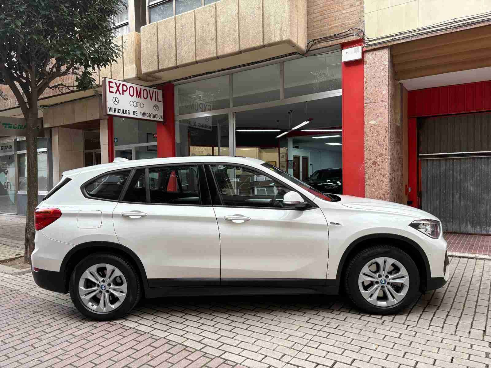 Un BMW X1 blanco está estacionado frente a un concesionario de automóviles.