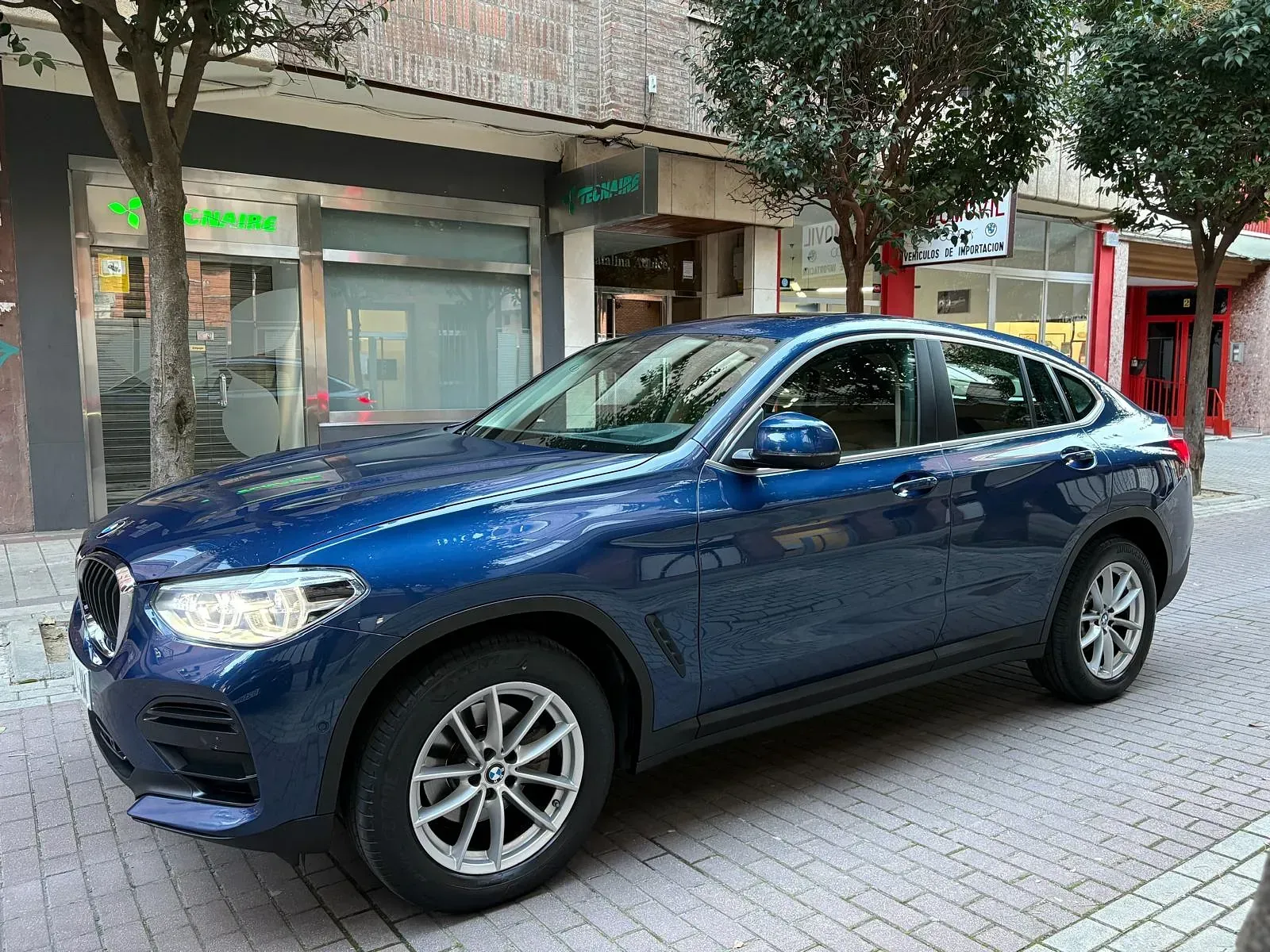 Un BMW X4 azul está estacionado al costado de la carretera frente a un edificio.