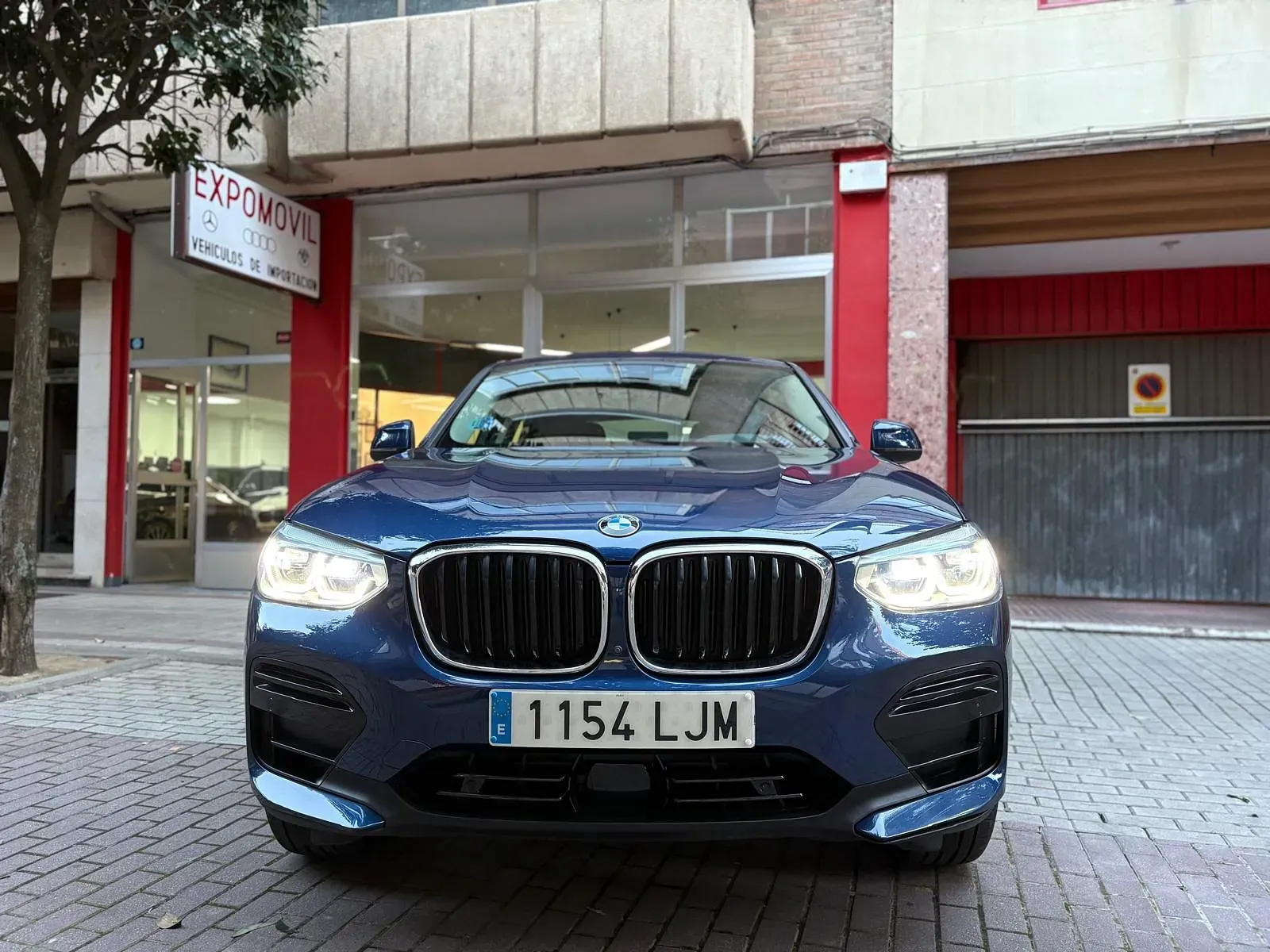 Un BMW azul está aparcado delante de un concesionario de coches.