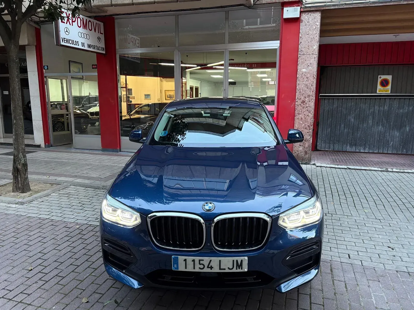 Un BMW X3 azul está estacionado frente a un concesionario de automóviles.