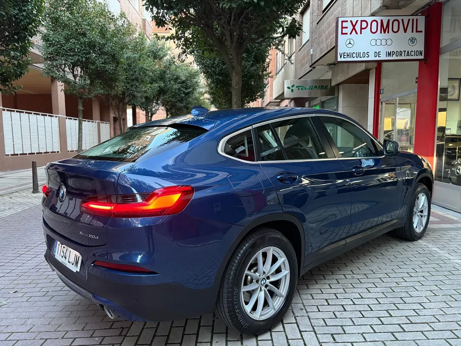 Un BMW X4 azul está estacionado frente a un concesionario de automóviles.