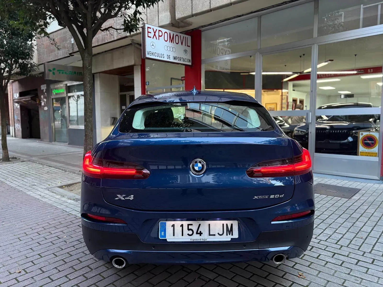 Un BMW X4 azul está estacionado frente a un concesionario de automóviles.