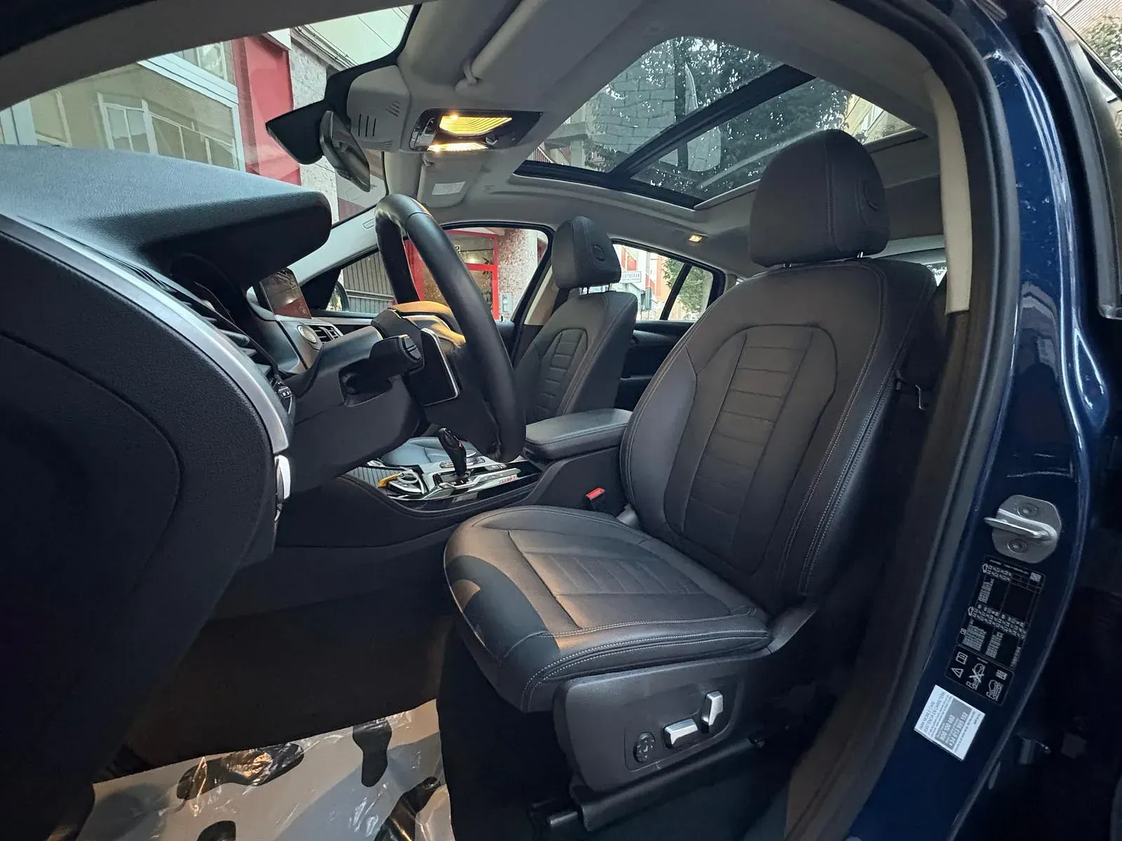 El interior de un coche azul con asientos de cuero negro y techo corredizo.