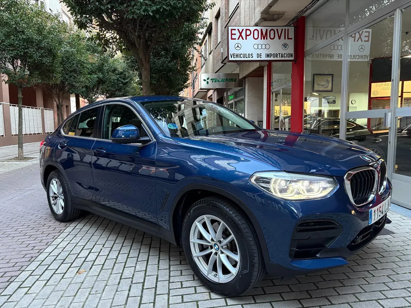 Un BMW X4 azul está estacionado frente a un concesionario de automóviles.