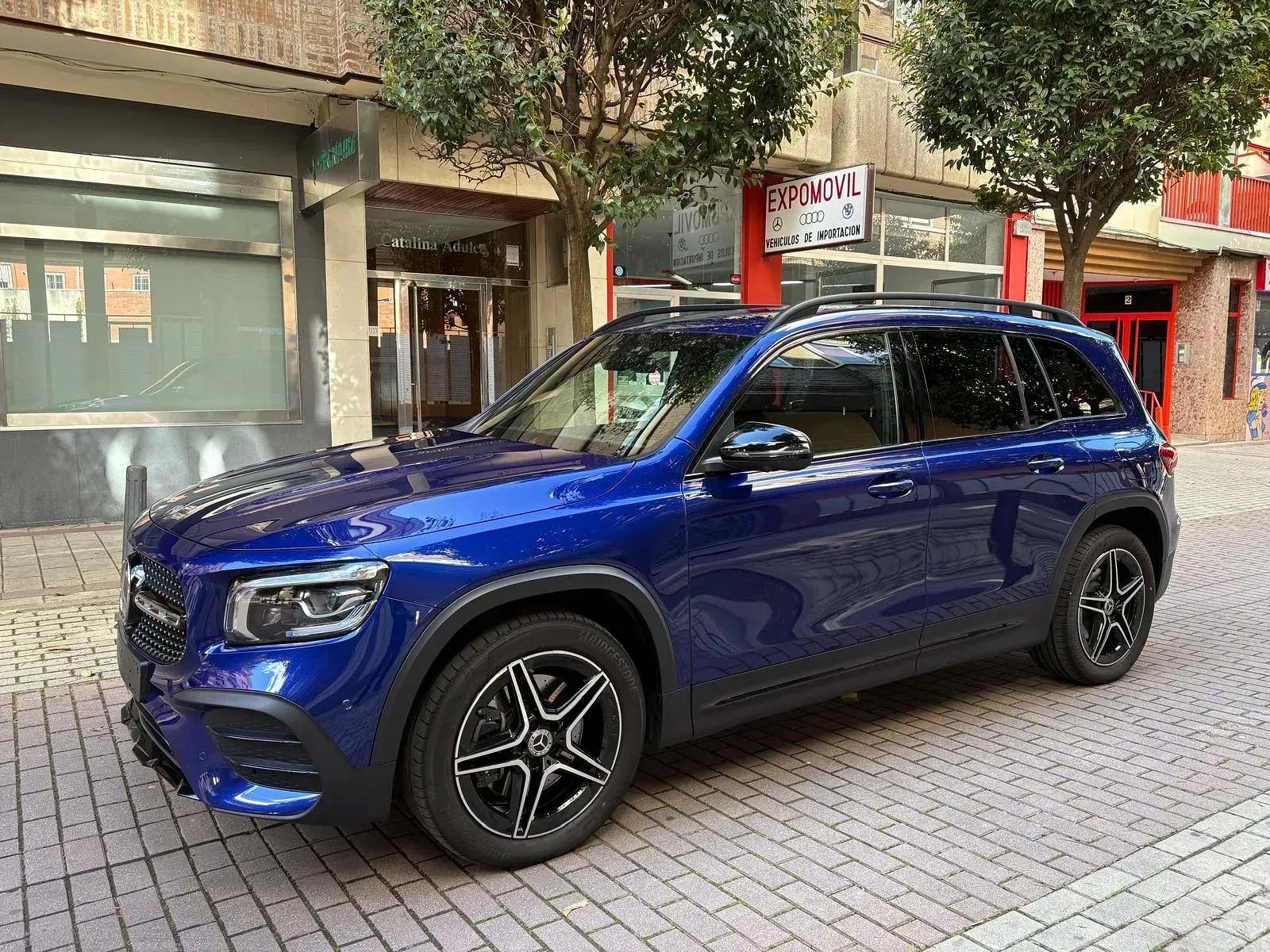 Una camioneta azul está estacionada en una acera de ladrillos frente a un edificio.